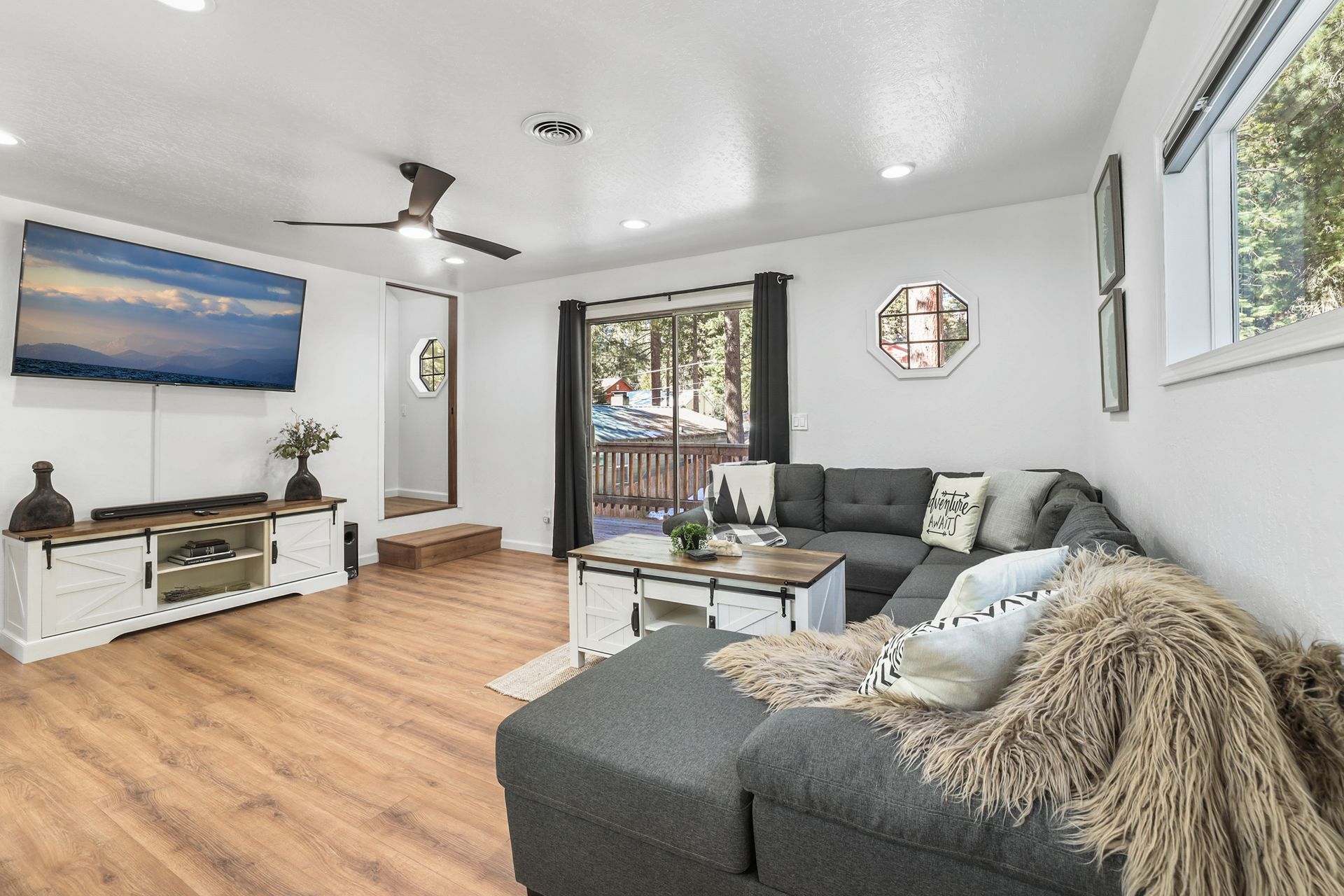 Bright living room with gray sectional sofa, wall TV, wood floors, and sliding glass door to a balcony