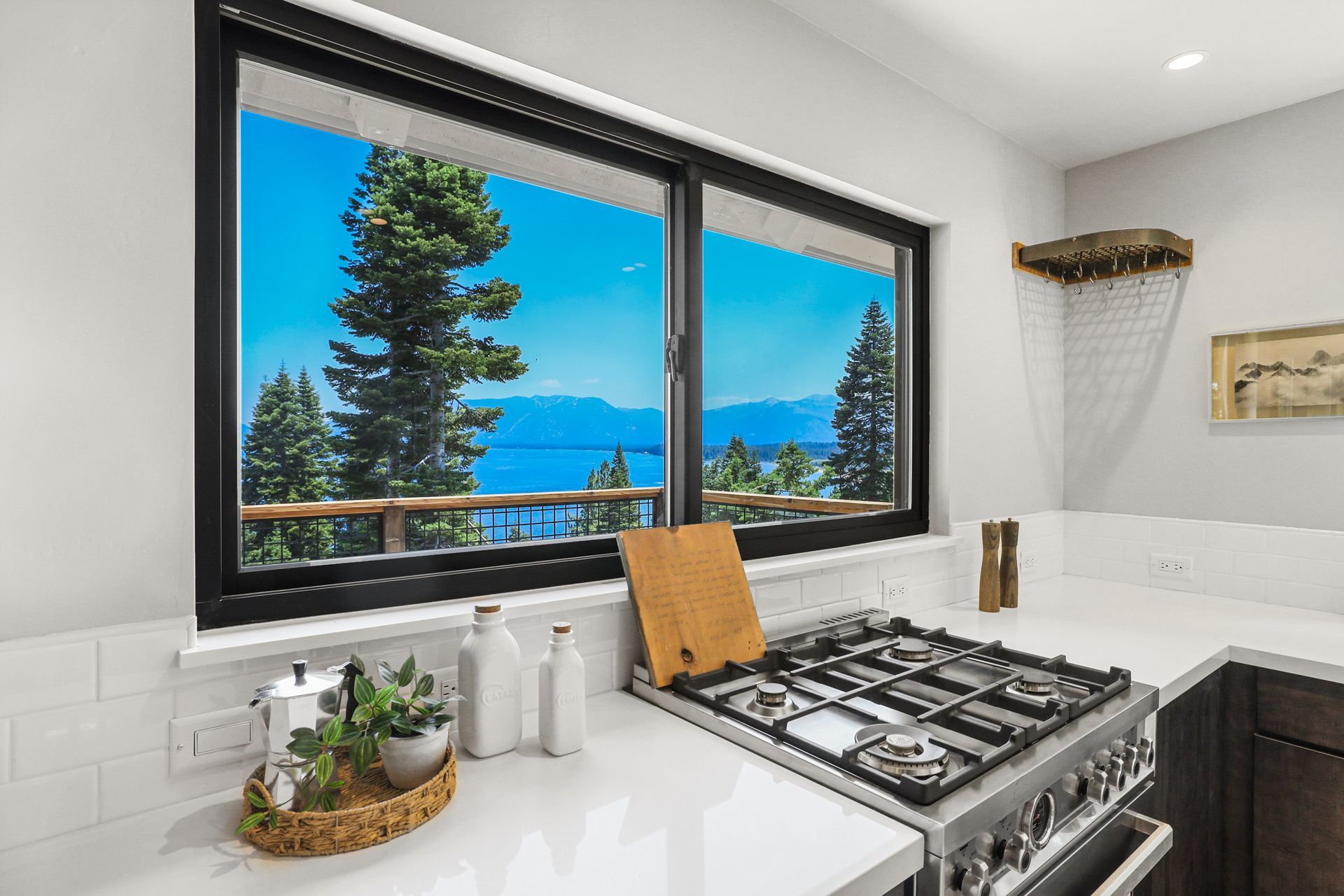 Modern kitchen with large window overlooking a lake and trees, stainless gas range, and white countertops