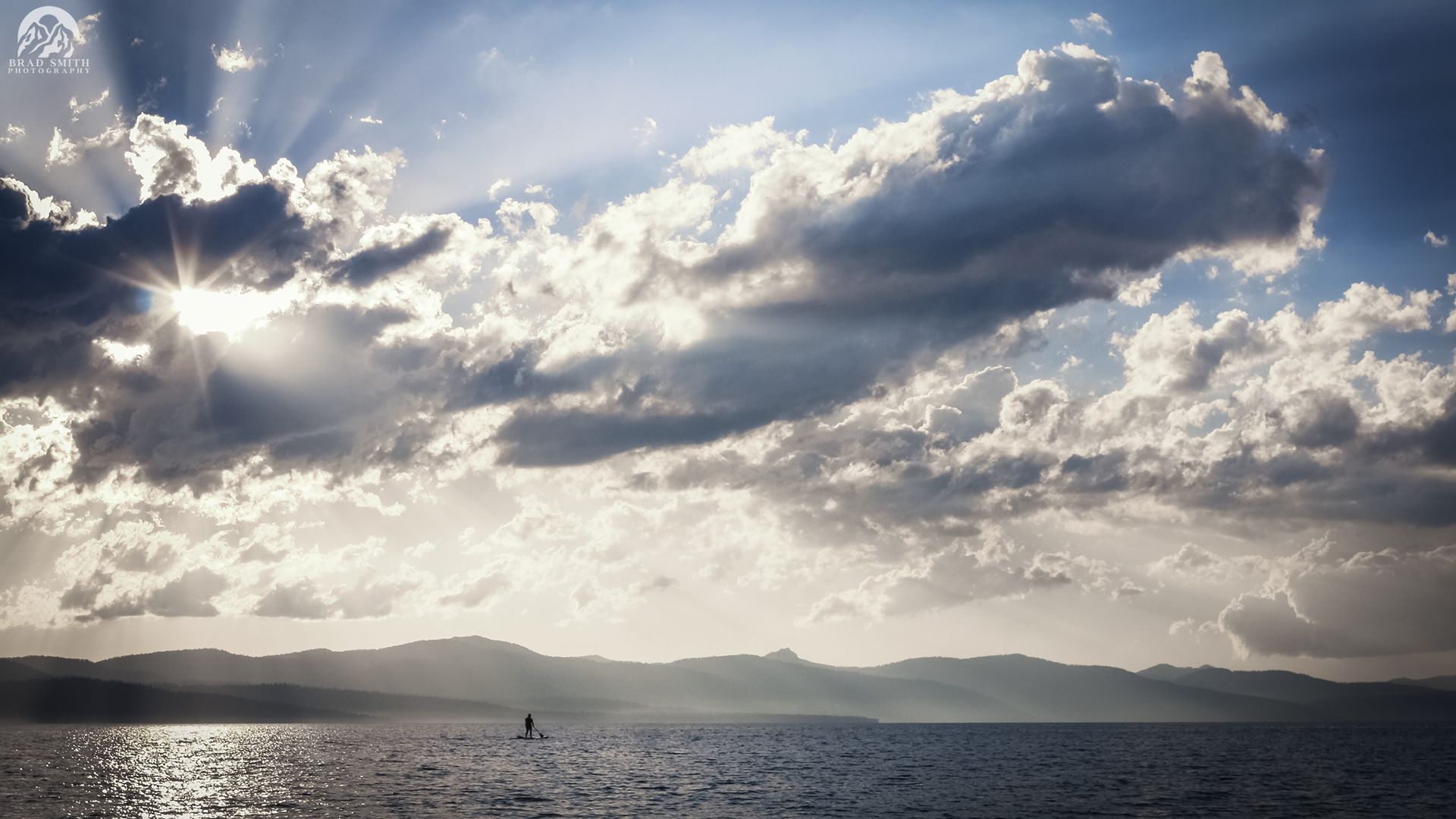 Sunlit ocean under dramatic clouds, with a distant coastline on the horizon