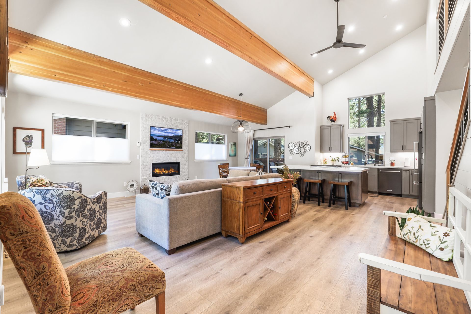 Bright open living room with vaulted wood beams, gray sofa, dining table, and large windows