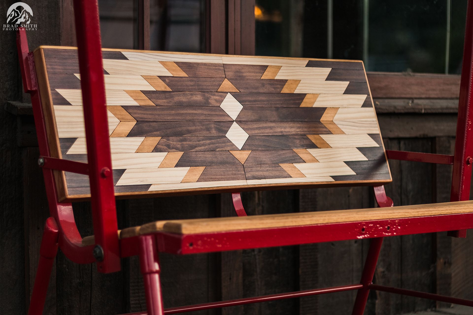 Wooden geometric pattern on a red bench against a rustic outdoor backdrop