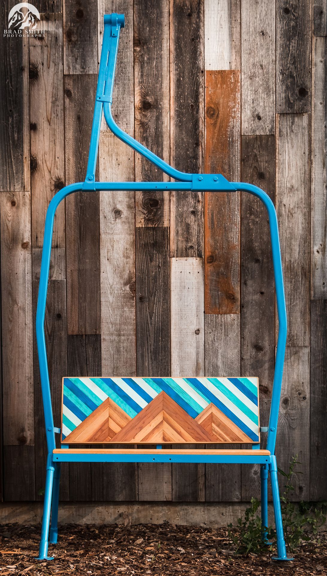Blue metal ladder with a colorful geometric wooden sign against a weathered wood wall