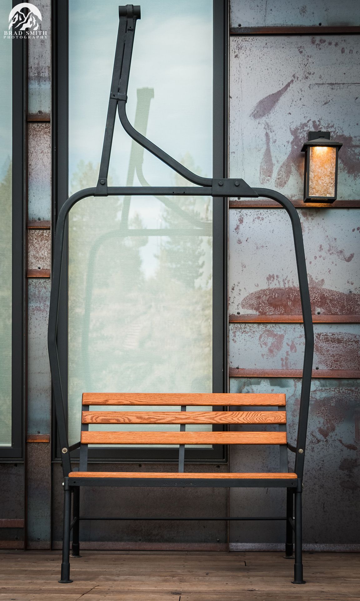 Empty black-framed bench with orange slats against a window and wall lamp in a rustic interior.