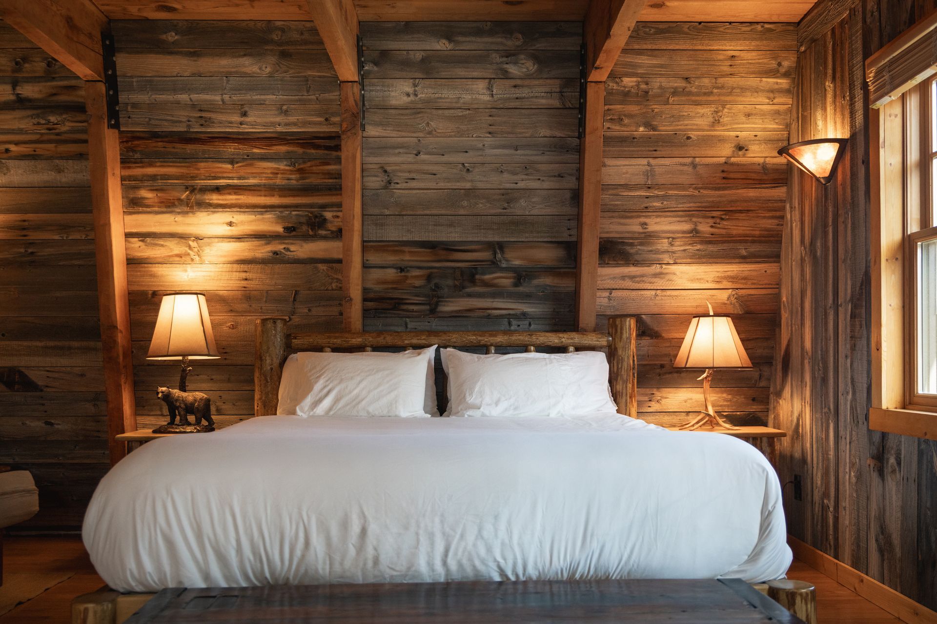 Rustic wood-paneled bedroom with a white bed, bedside lamps, and warm ambient lighting.