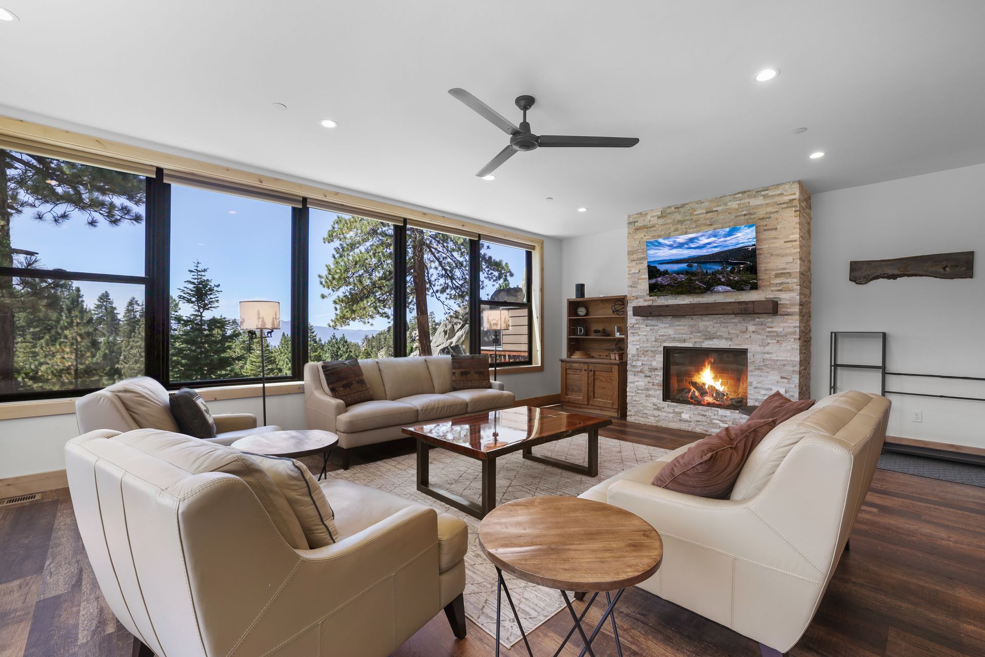 Bright living room with large windows, beige seating, stone fireplace, and mountain views