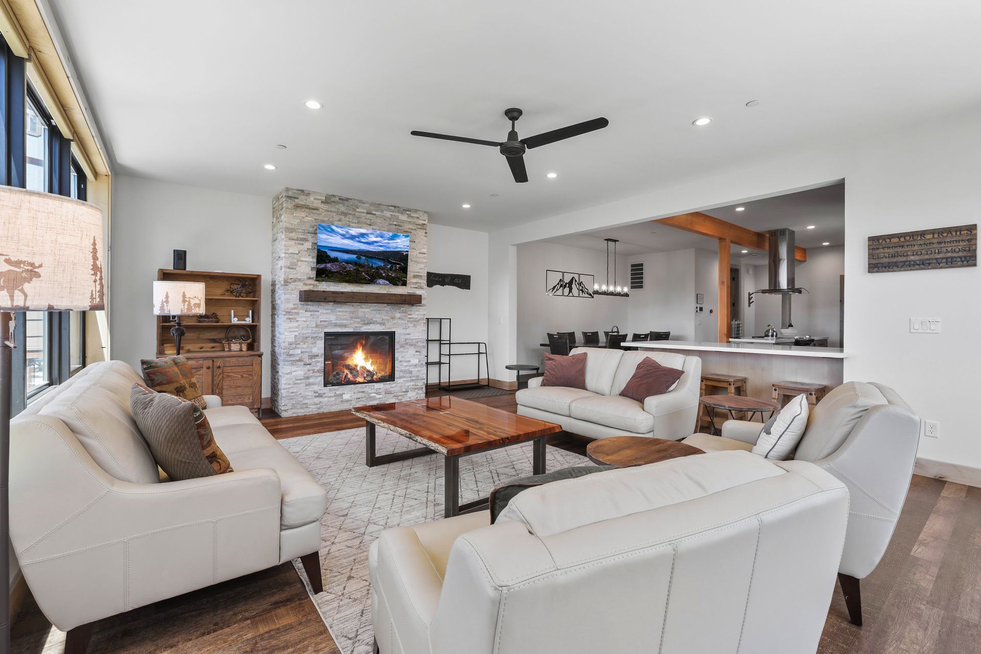 Bright modern living room with white sofas, fireplace, TV, and open kitchen.