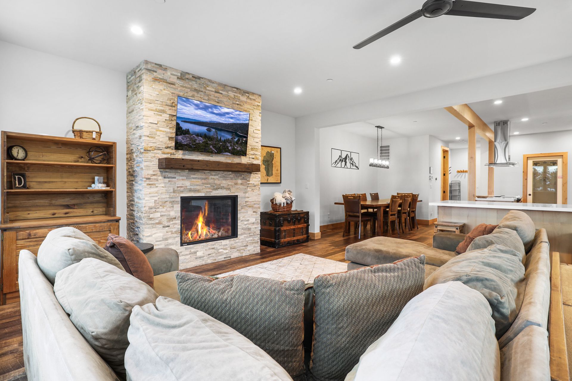 Cozy living room with stone fireplace, wall-mounted TV, sectional sofa, and adjacent dining area