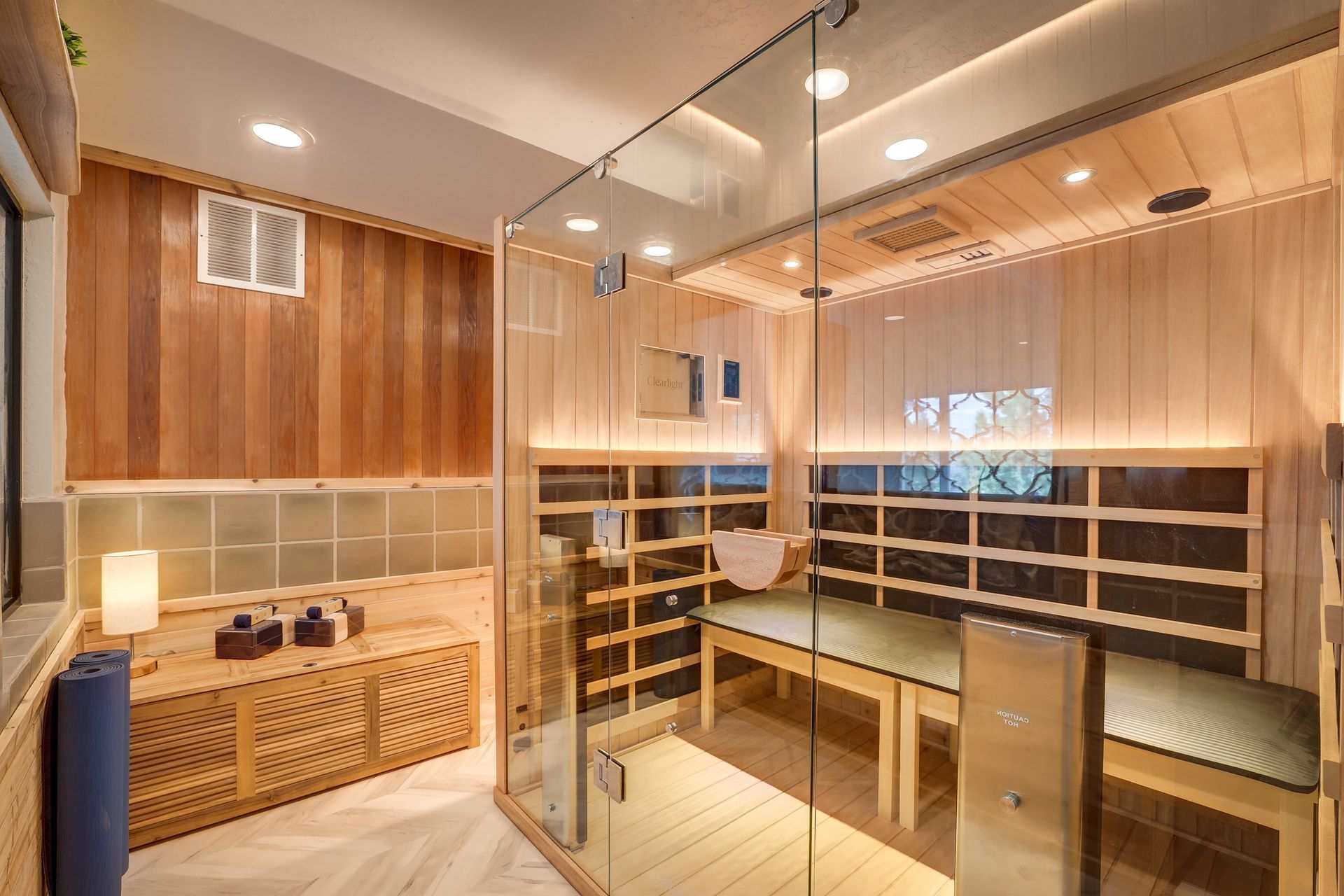 Modern wood-paneled sauna with glass walls, benches, and warm lighting