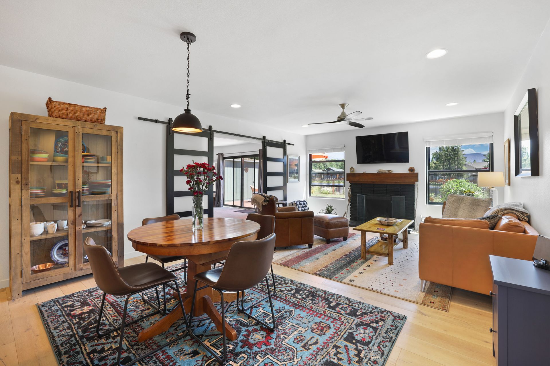 Bright open living-dining room with fireplace, TV, leather sofa, round table, rugs, and large windows