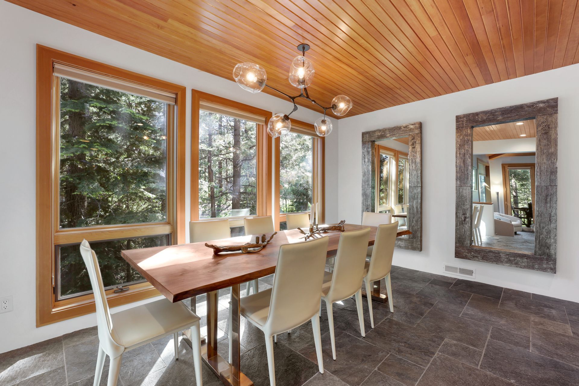 Dining room with wooden ceiling, large windows, and a dining table with chairs by the fireplace