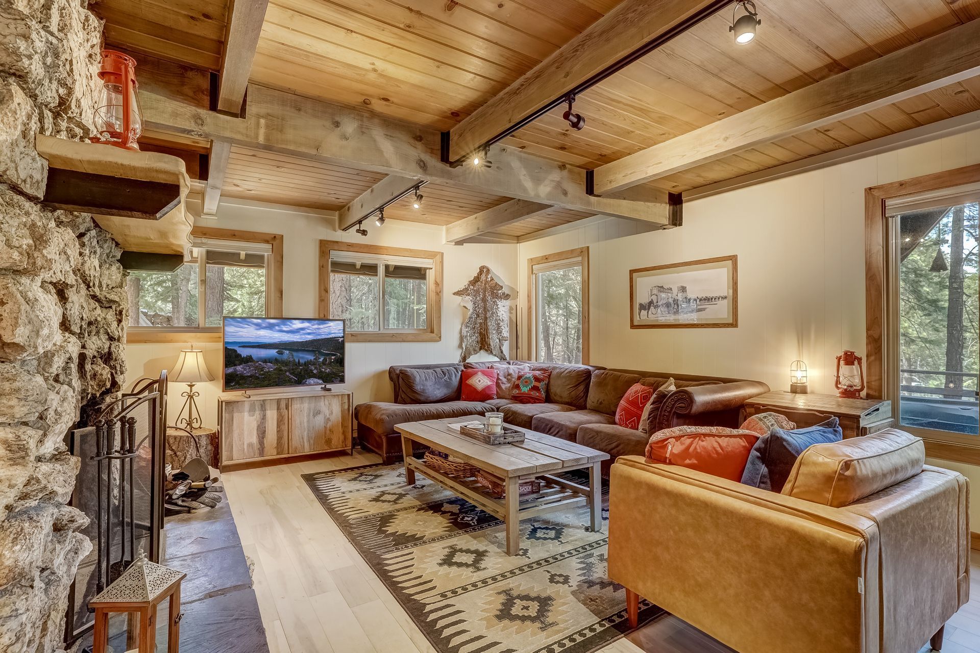 Cozy log cabin living room with stone fireplace, wooden beams, sectional sofa, and large windows