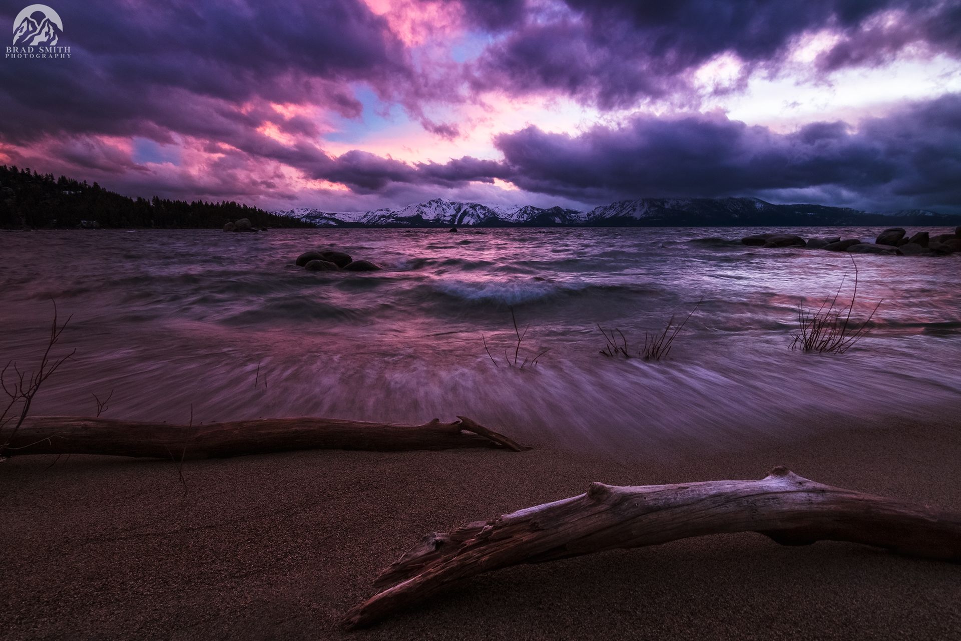Stormy purple sunset over a beach with driftwood and rough waves under dark clouds