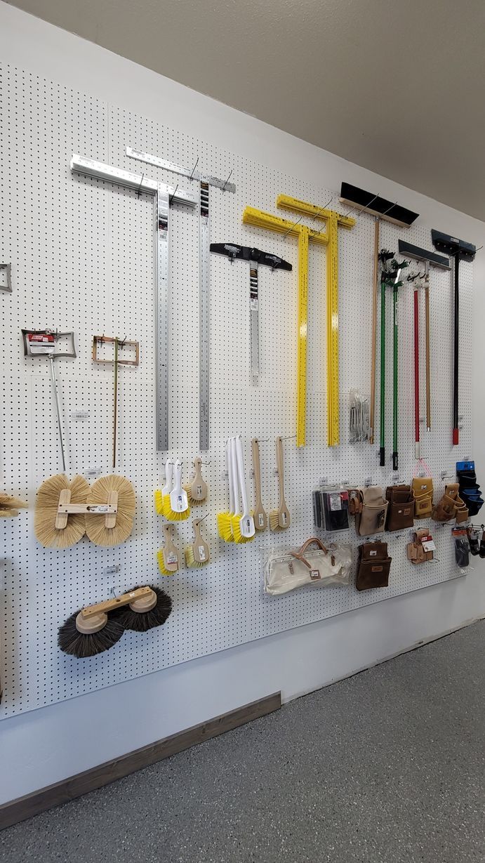 Tools organized on a pegboard wall in a garage, including brooms, squeegees, and brushes.