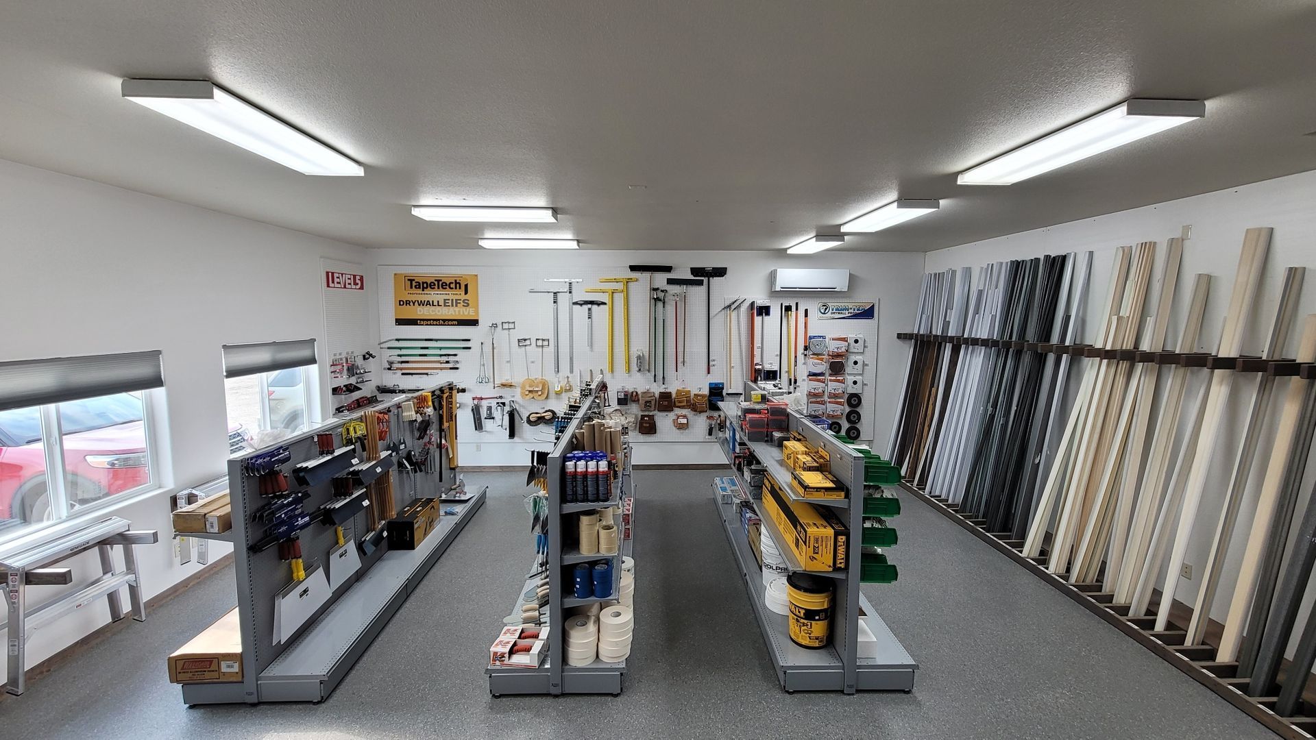 Hardware store interior with tools on shelves and trim samples on a wall.