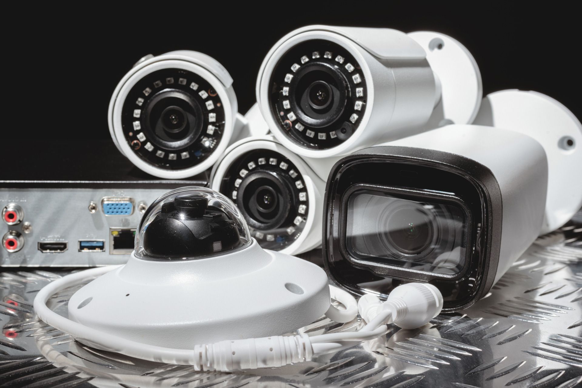 Three different kinds of security cameras on a metal sheet against a black background