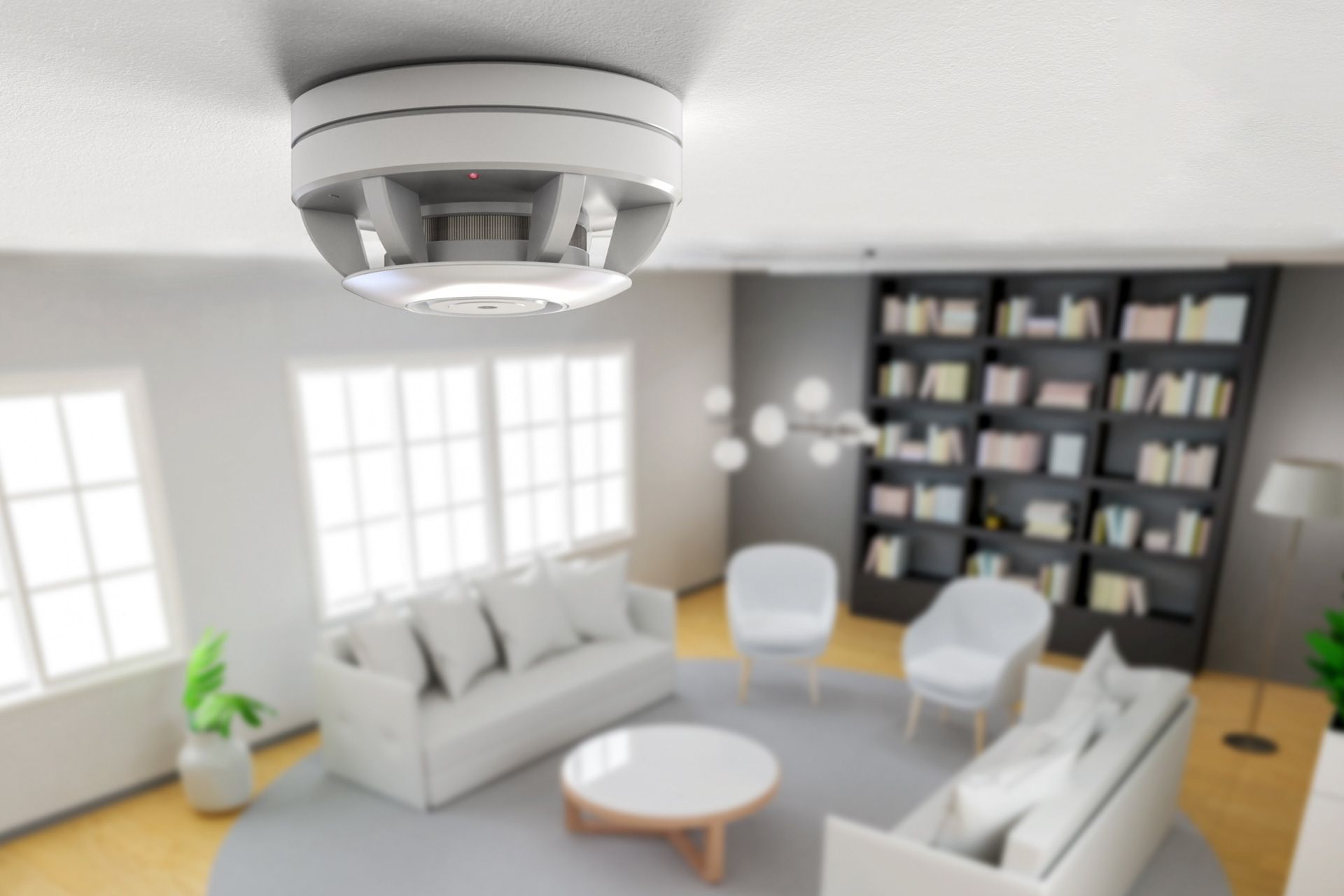 A smoke detector attached to the a living room ceiling with furniture in the background below