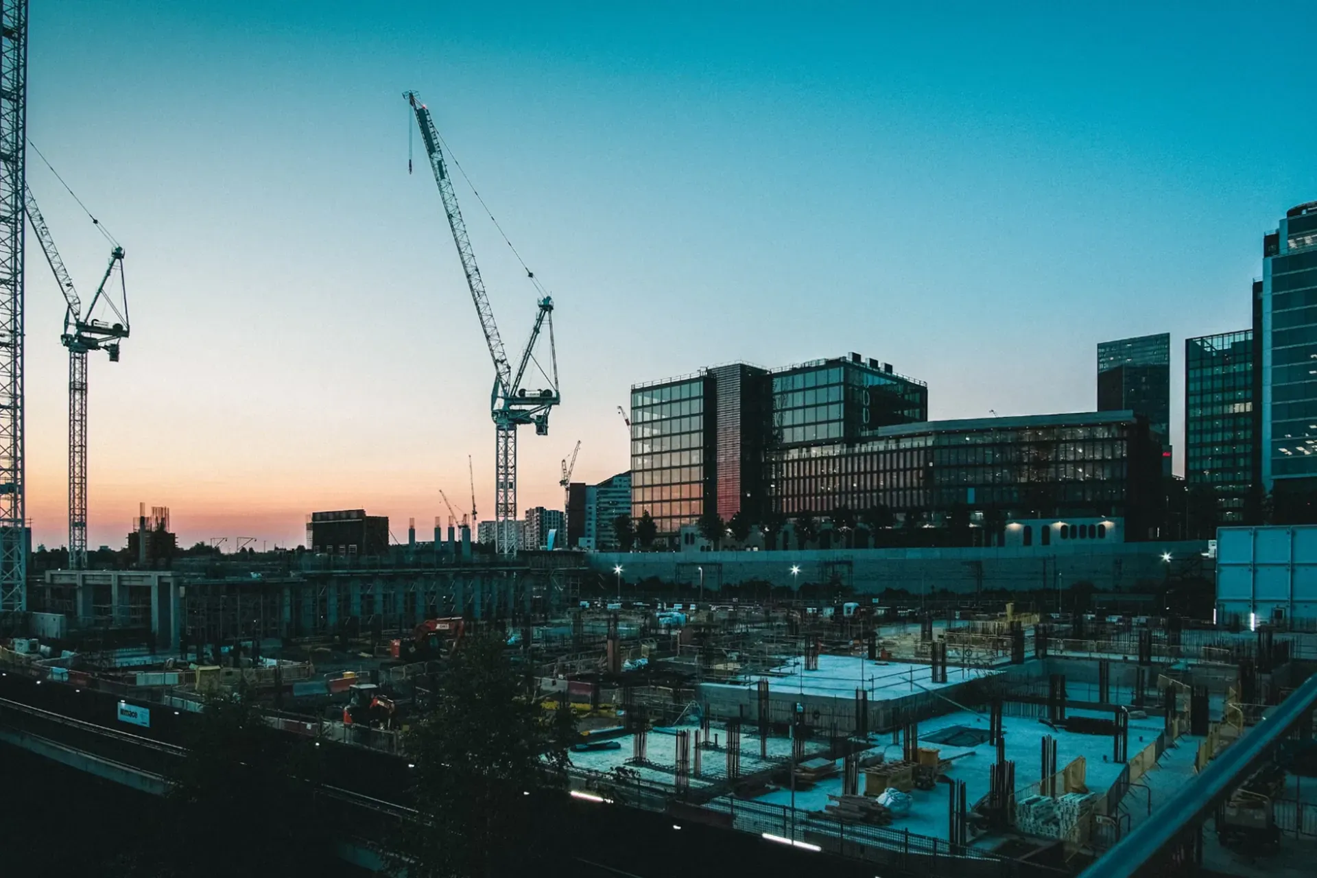 An evening sky over a construction site with cranes near glass buildings