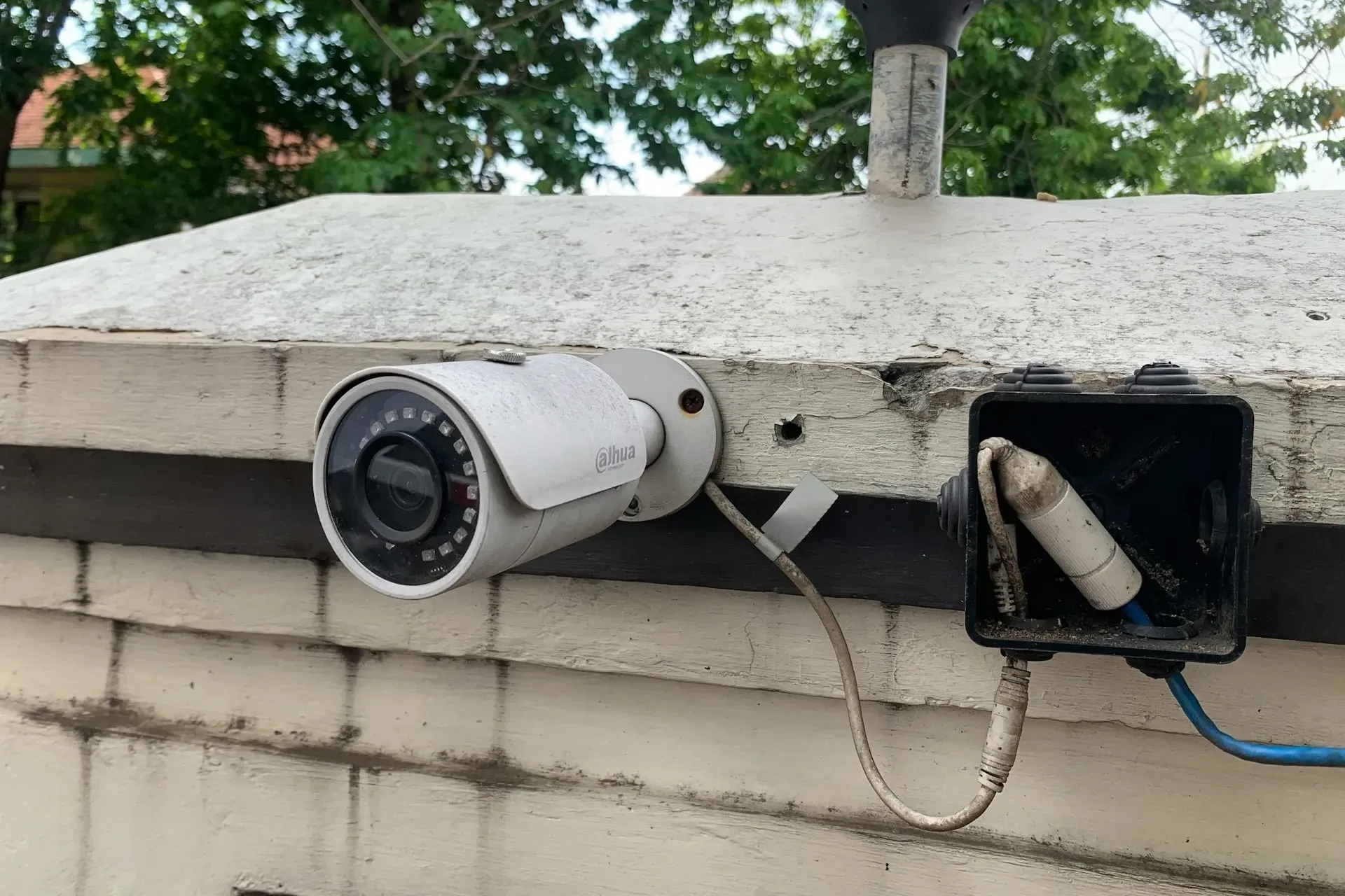An outdoor wired security camera attached to a brick fence.