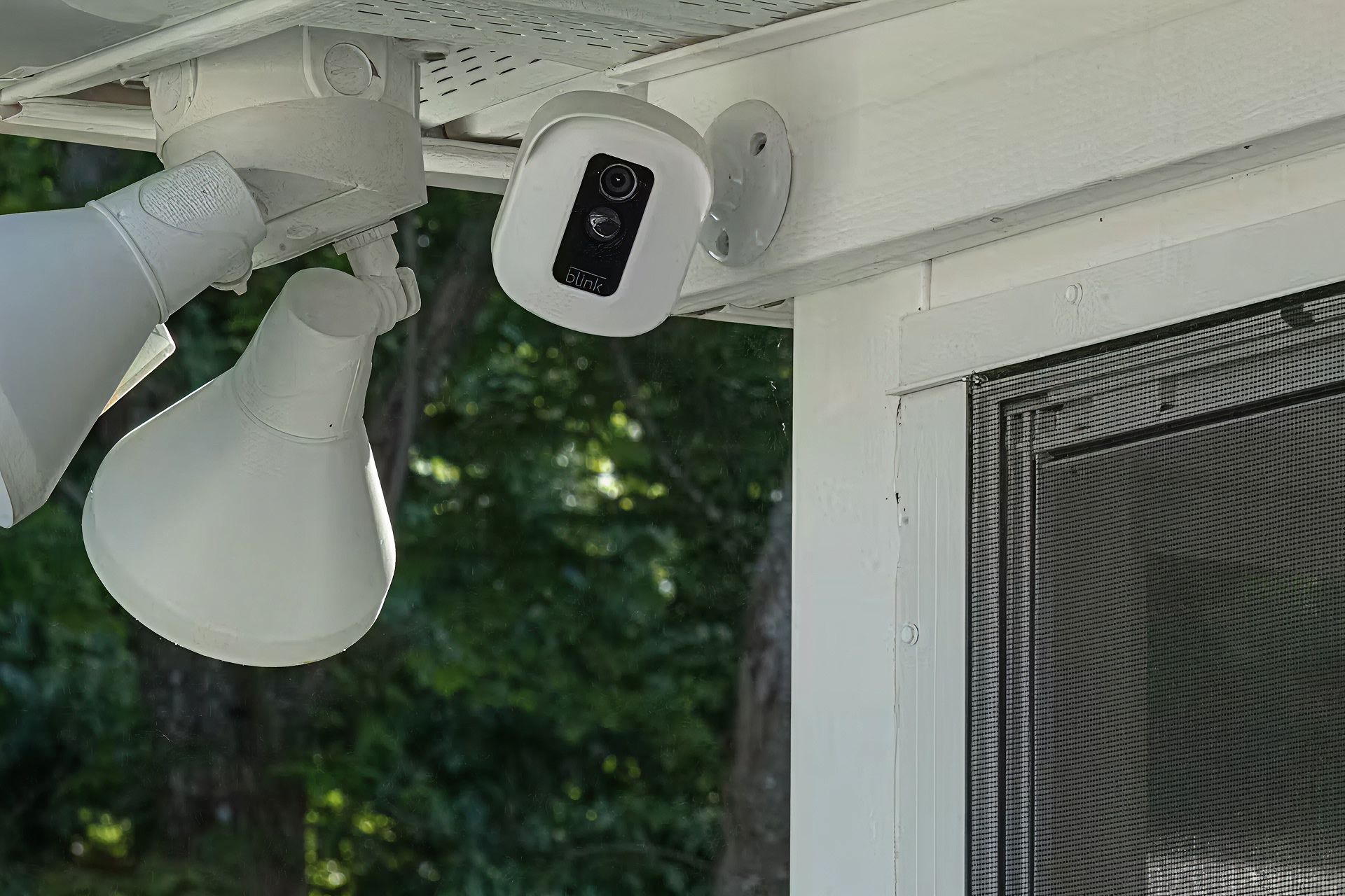 A security camera is hoisted above a house door next to porch lights