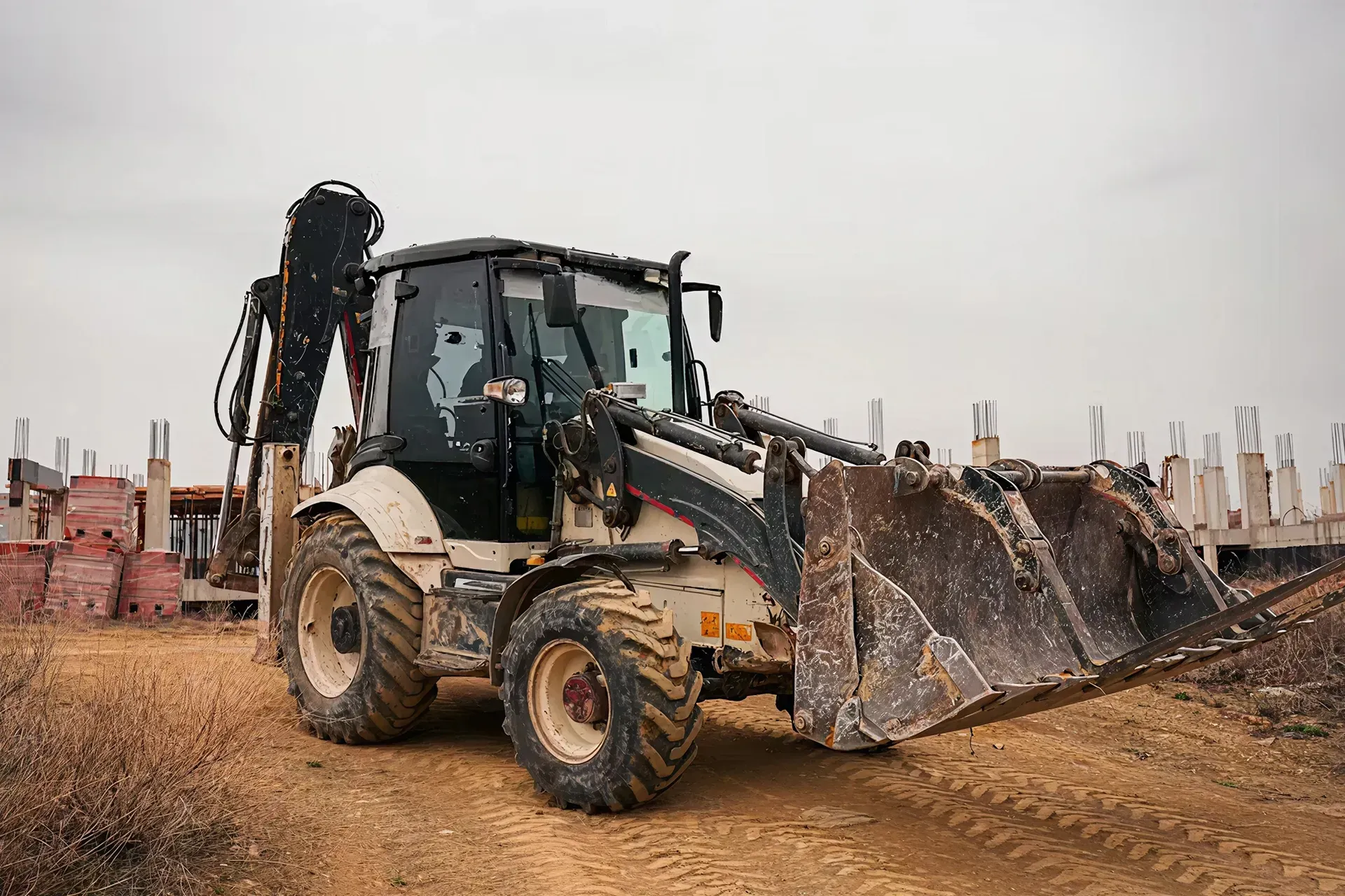 An excavator moves along a mud patch on a site with concrete beams.