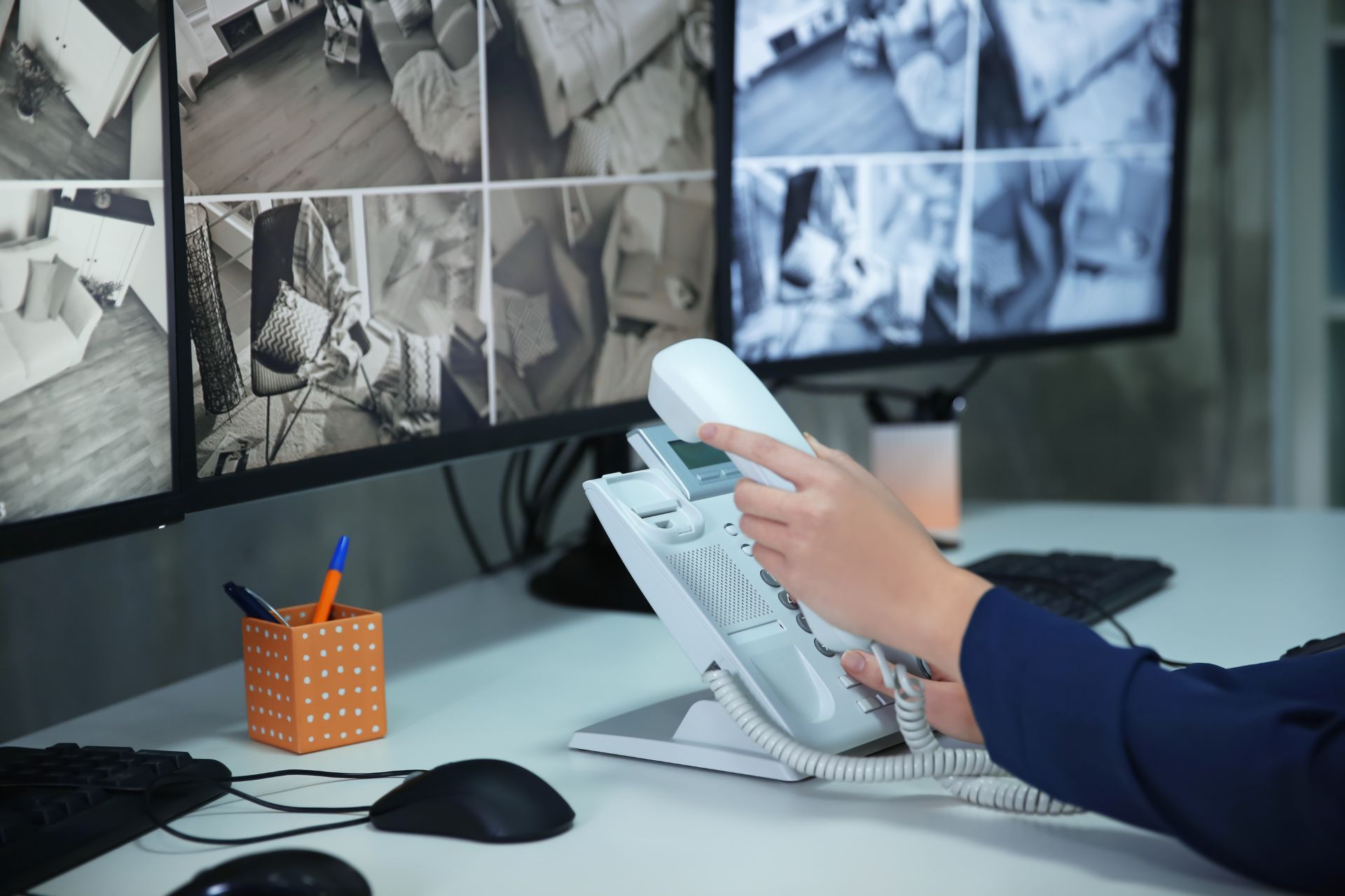 Someone holding a corded phone and sitting at a desk with a large screen showing multiple security camera feeds