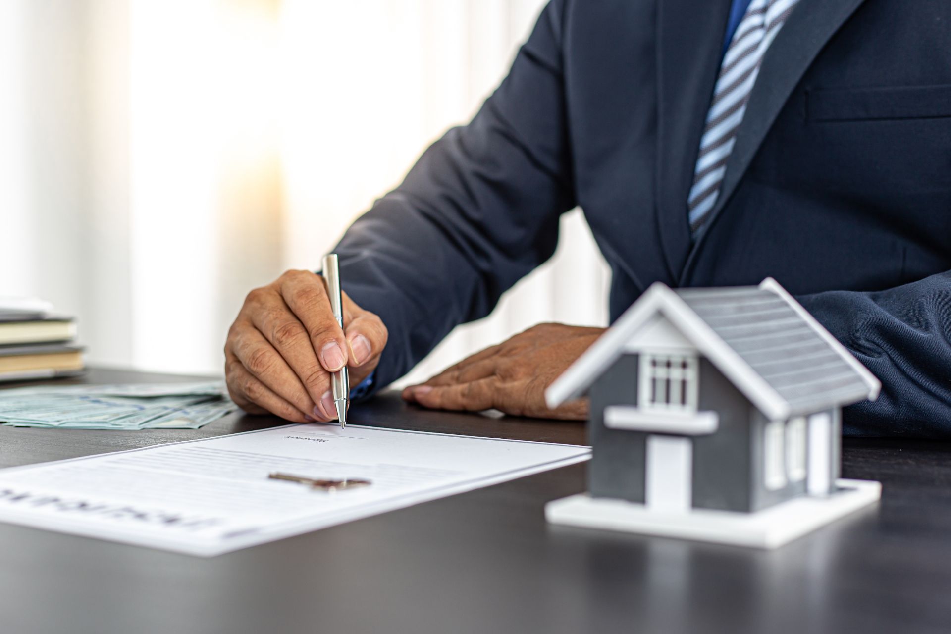 A person signing a home insurance policy at a desk with a small model of a house on it