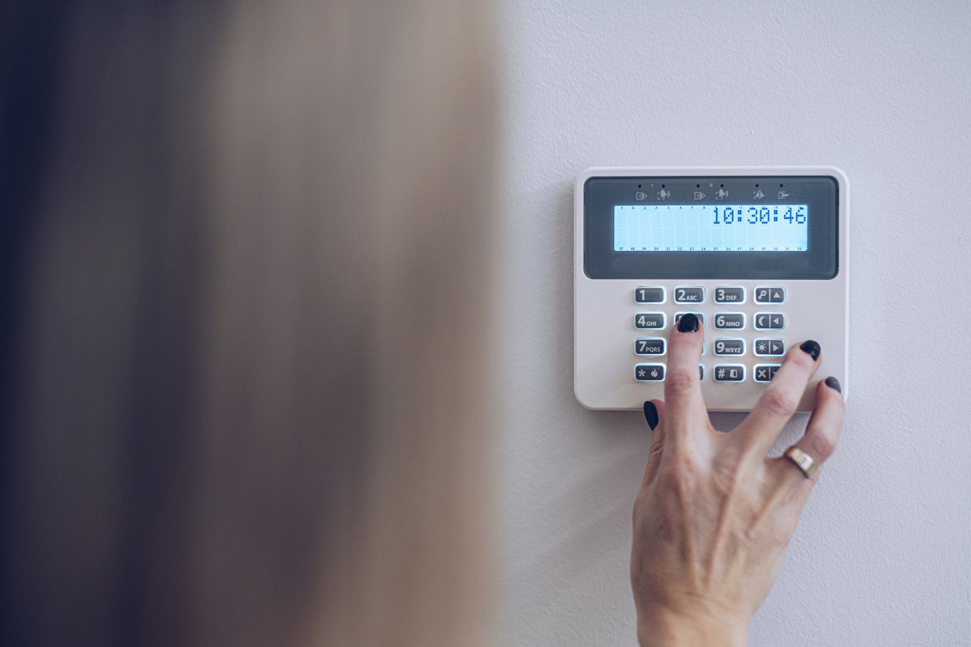 Close-up of a person's hand entering a code into a keypad on a home security control panel. 