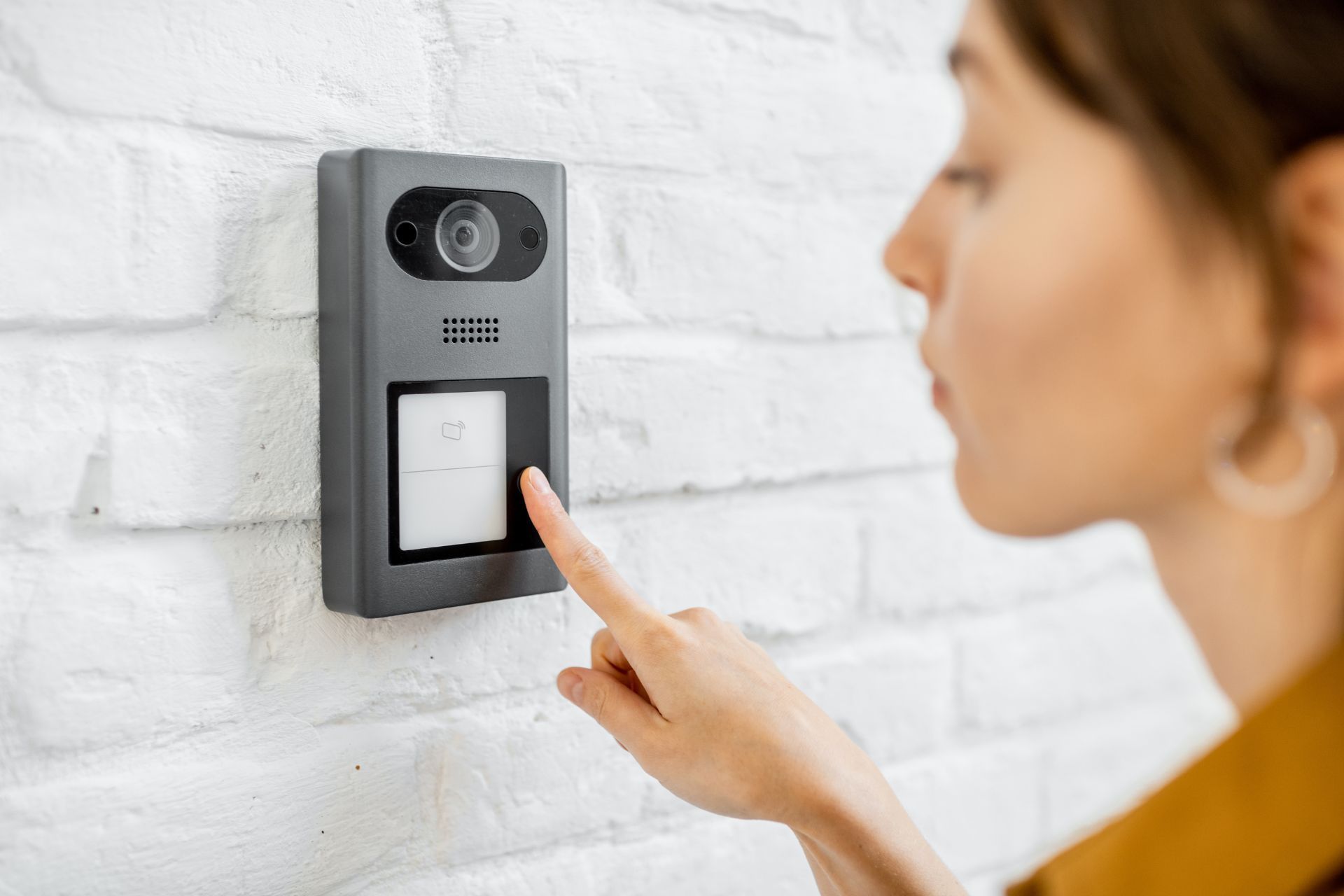 A woman pressing a button on a video doorbell
