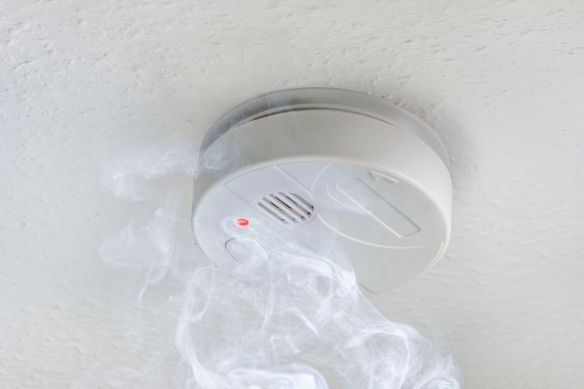 White smoke detector on the ceiling with smoke around it