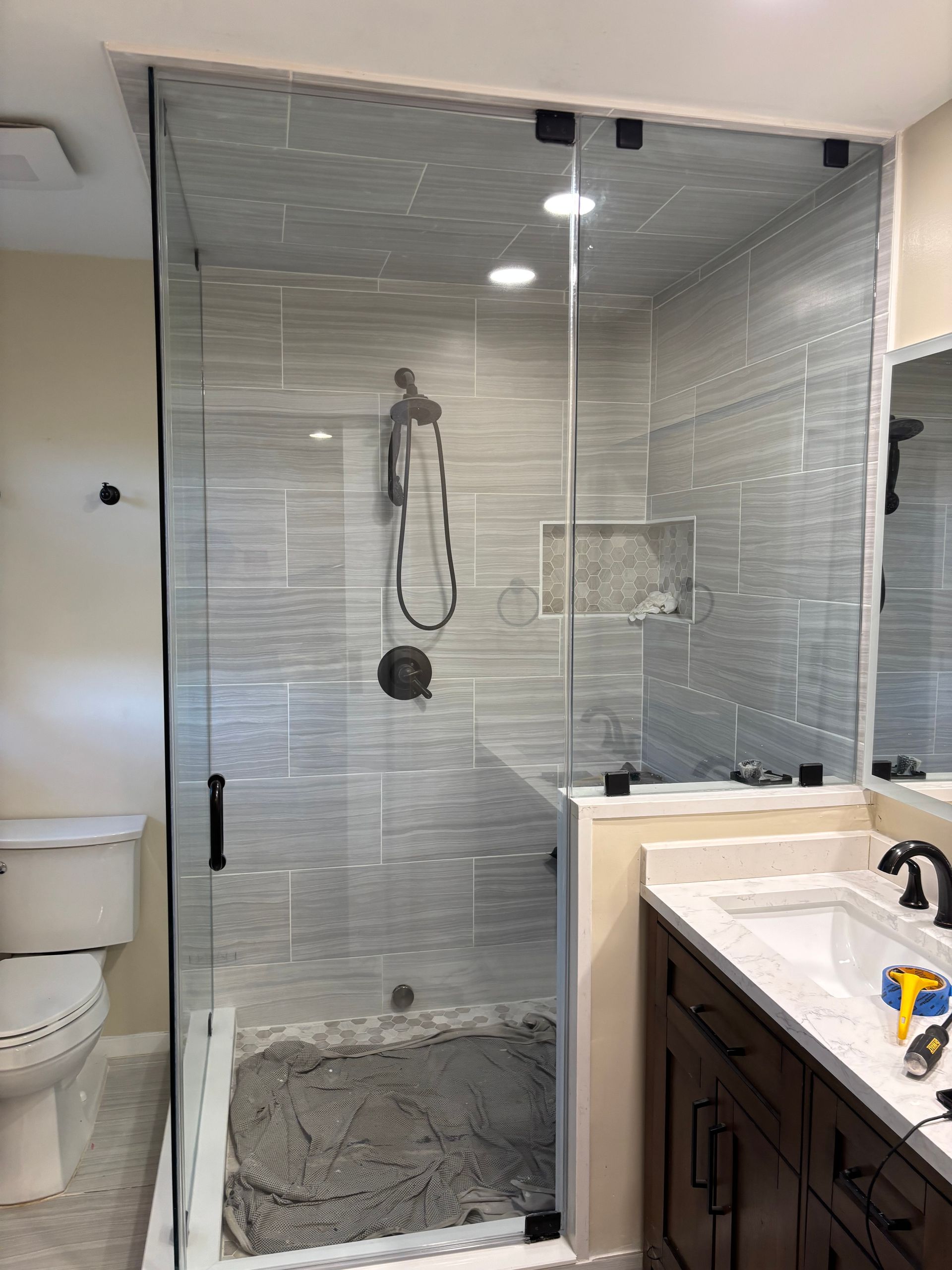 Glass shower enclosure with gray tiled walls in a renovated bathroom.