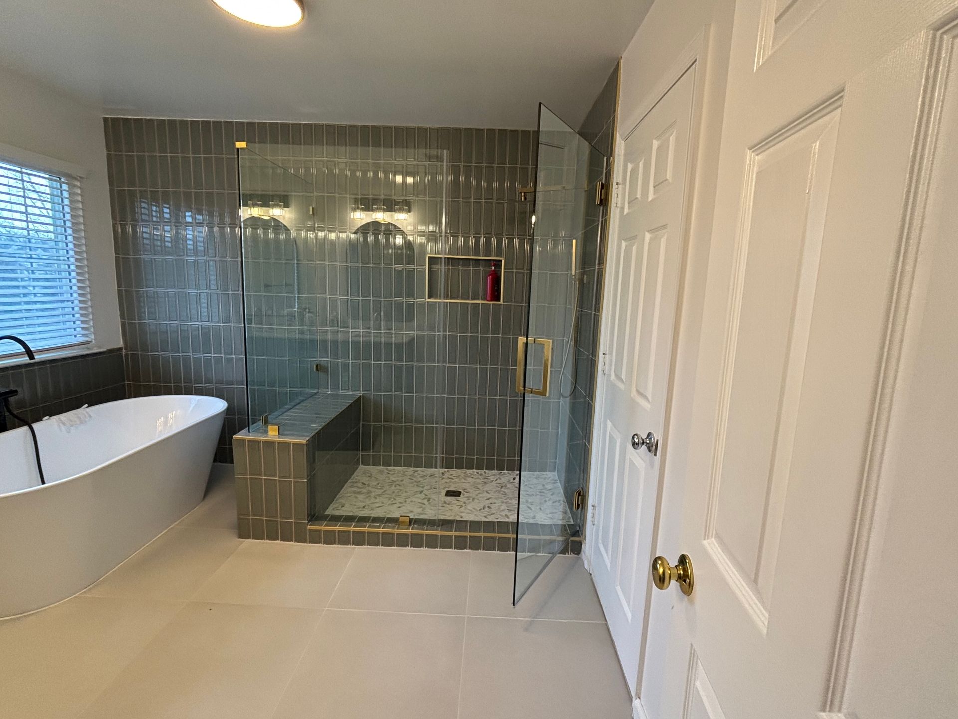Modern bathroom with a glass shower, soaking tub, and gray tile walls.