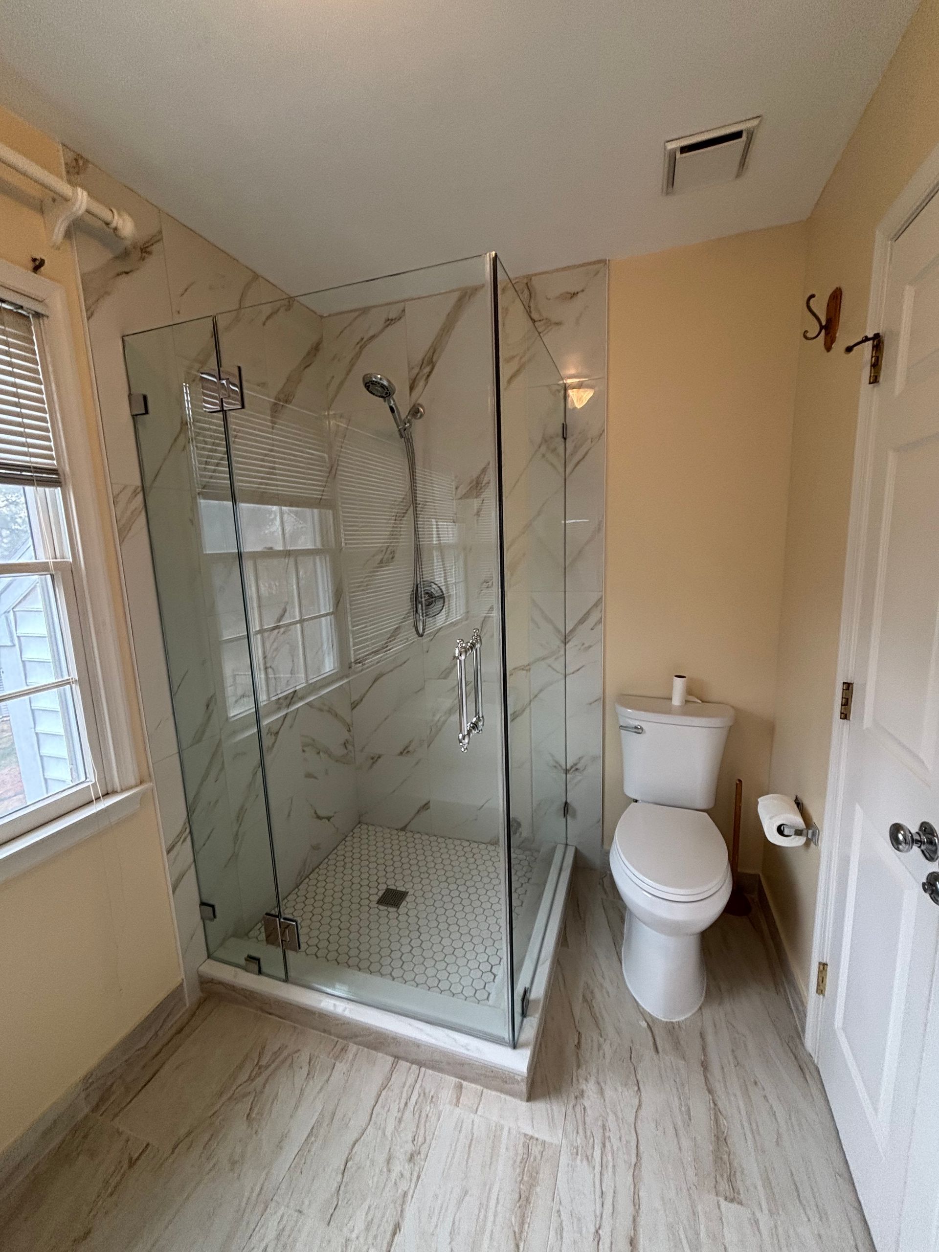 Bathroom with glass shower, white toilet, tan walls, and light-colored tile floor.