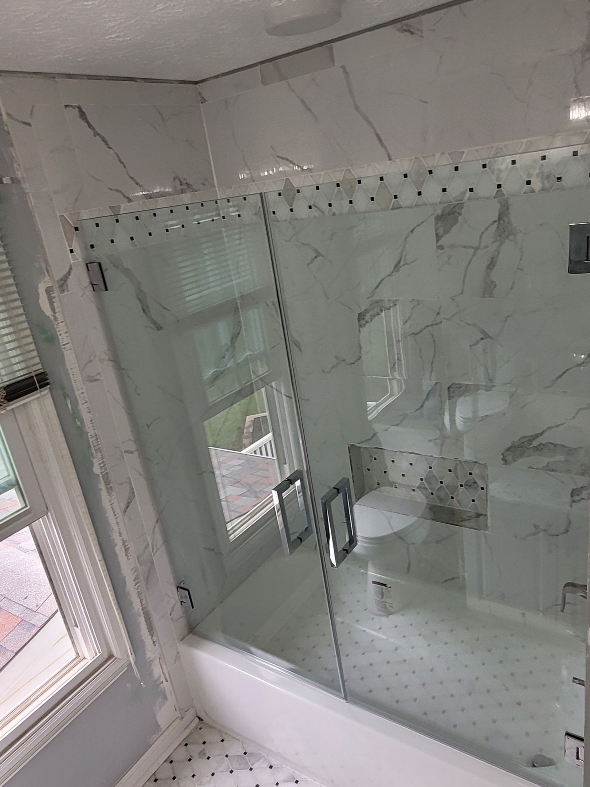 A bathroom with marble tiles and a glass shower door.