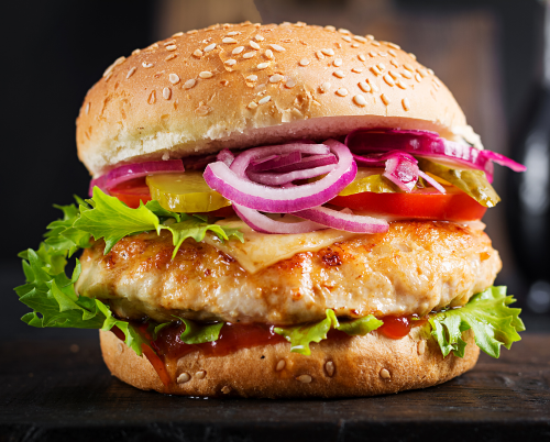 A chicken hamburger with lettuce , onions , tomatoes and pickles on a sesame seed bun.