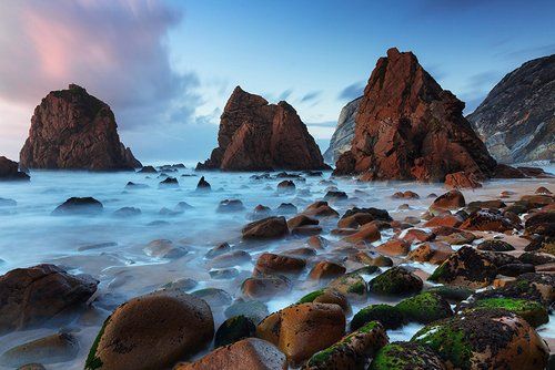 A rocky beach with a large rock in the middle of the water.