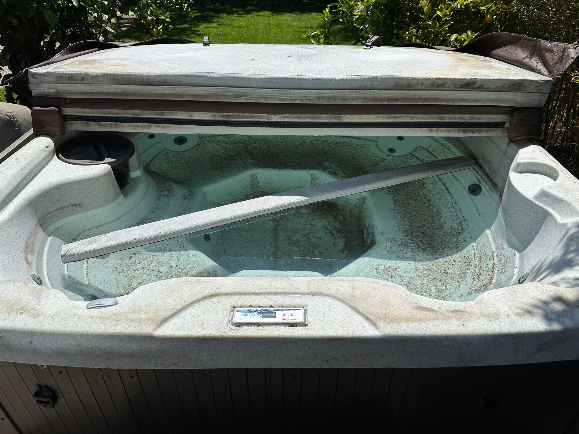 A dirty hot tub with the lid open in a backyard