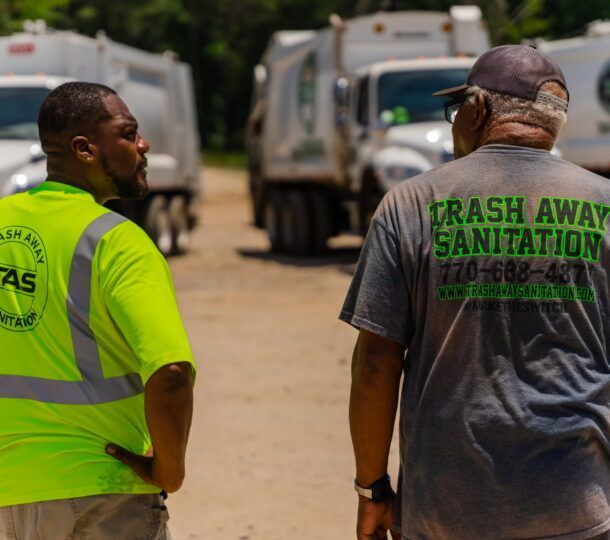 A man wearing a trash away sanitation shirt stands next to another man