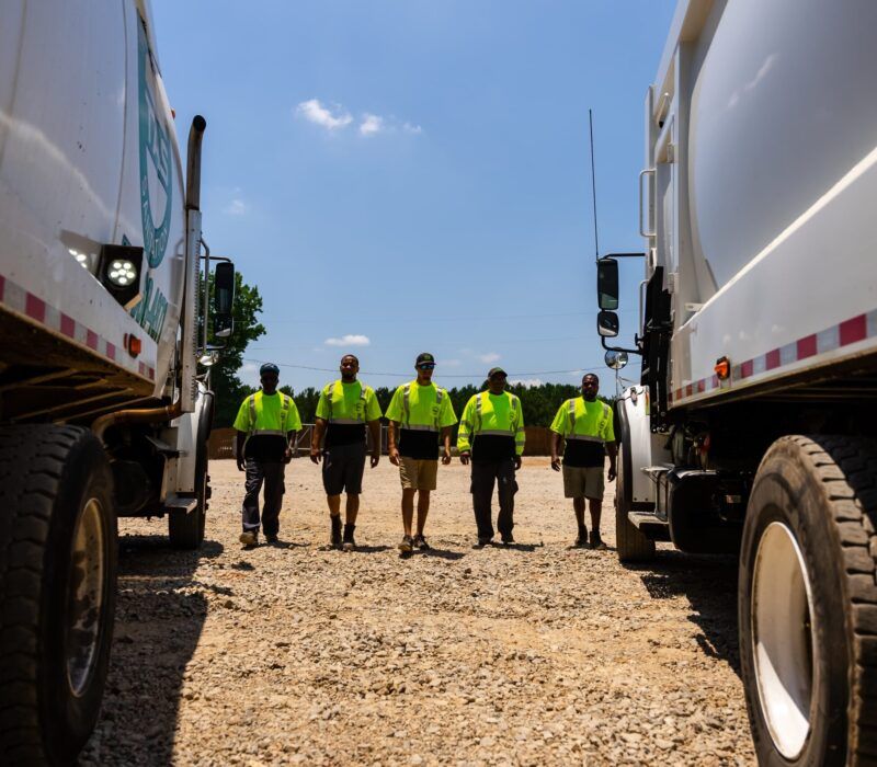 A group of men are standing in front of garbage trucks