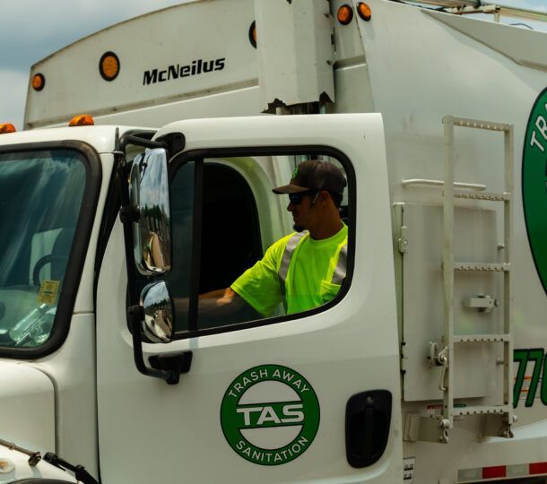A man is driving a trash away sanitation truck
