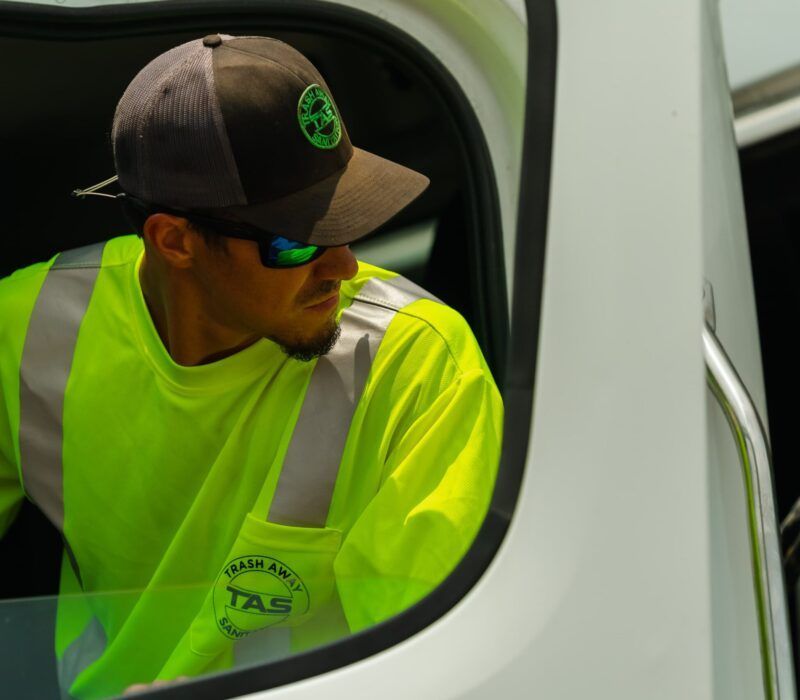 A man wearing a hat and sunglasses is looking out the window of a truck