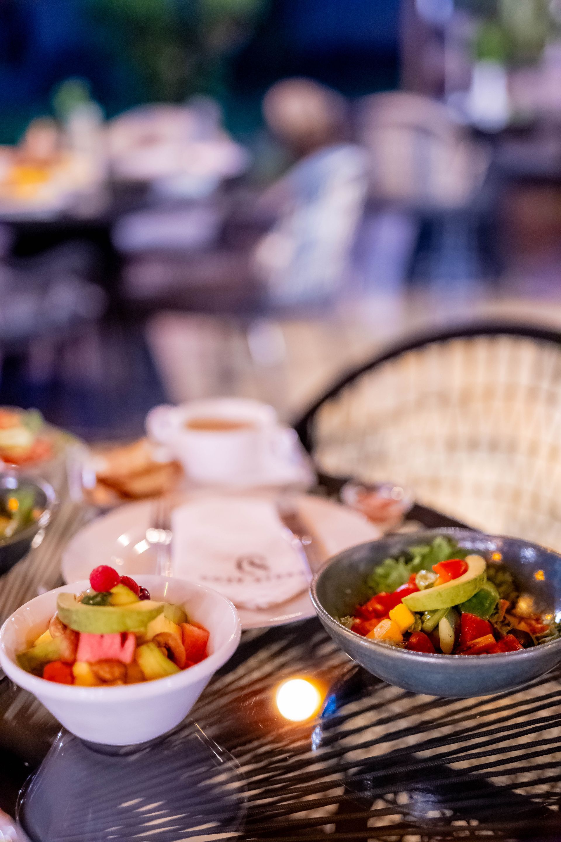 Bowls of colorful fruit salad and other dishes on a table, blurred restaurant background.