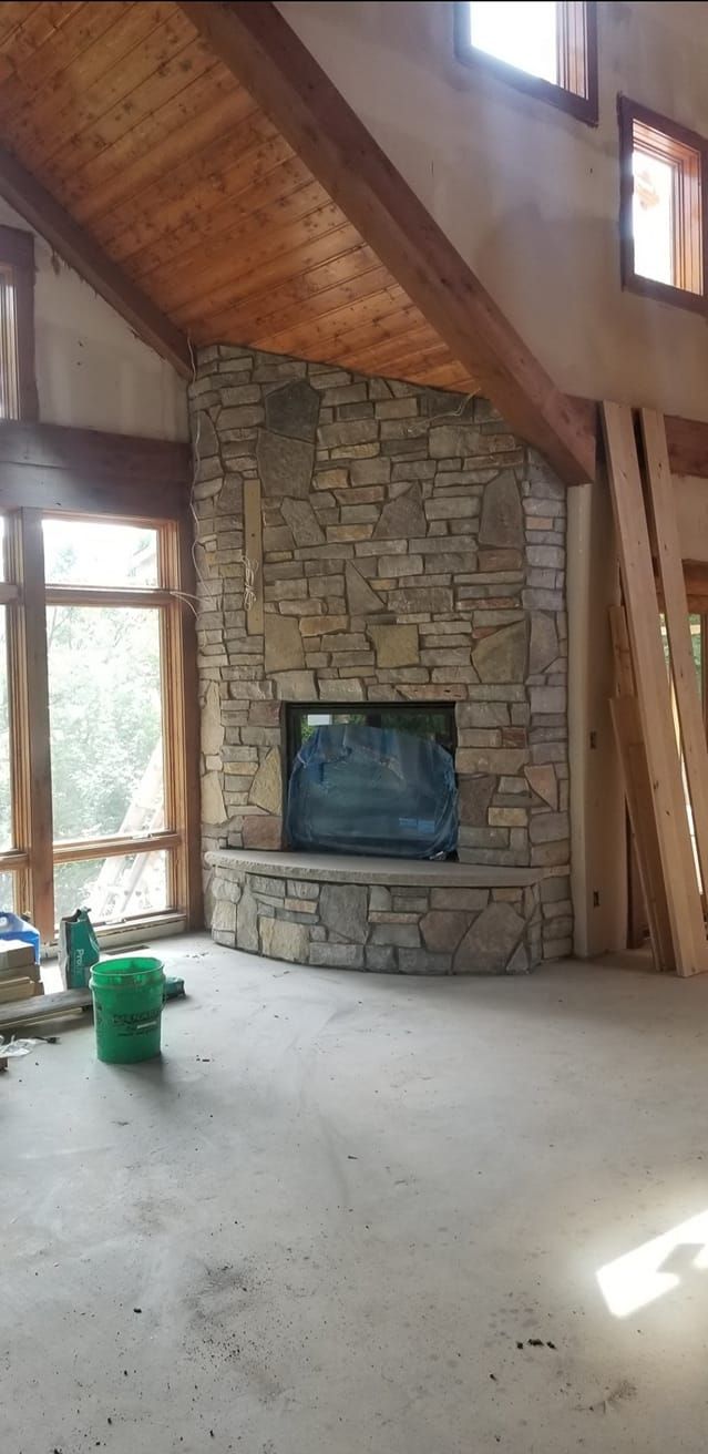 A living room with a stone fireplace and a wooden ceiling.