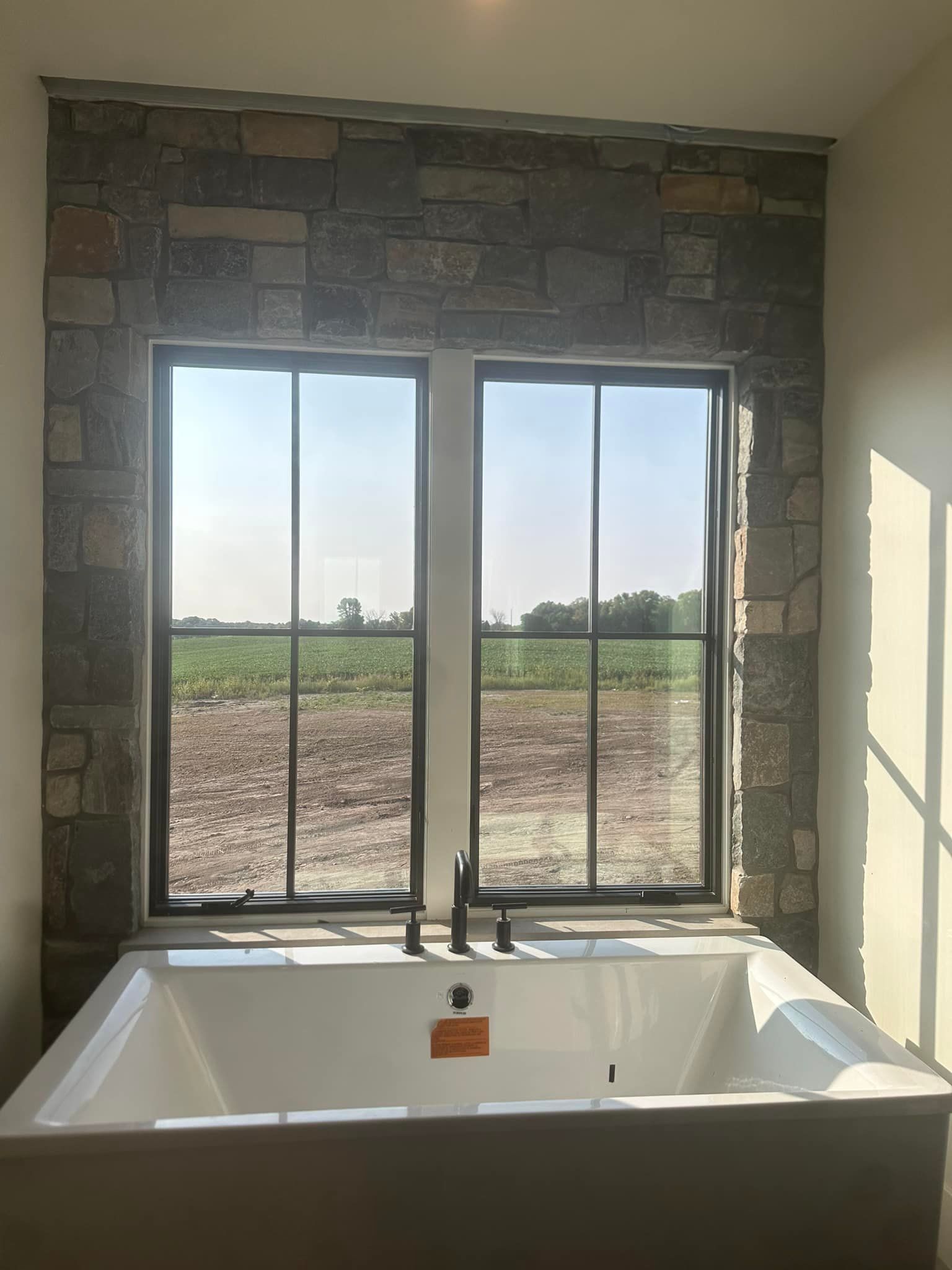 A bathtub in a bathroom next to a window with a view of a field.