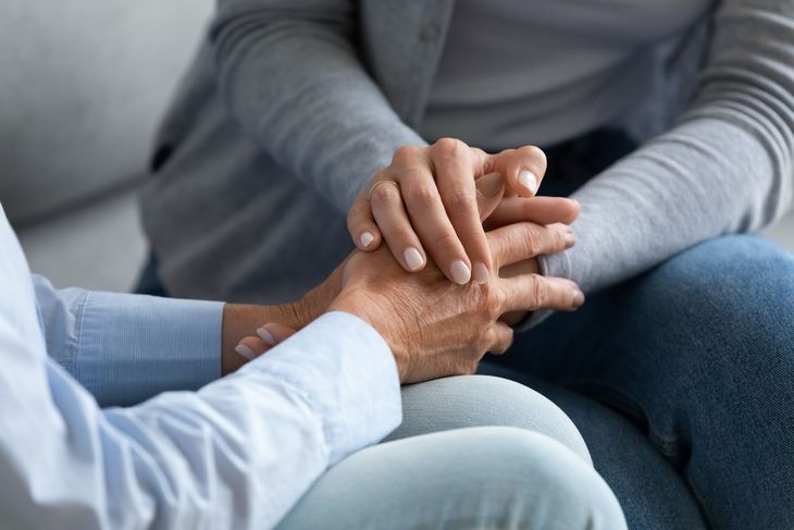 Two people holding hands in a supportive conversation indoors