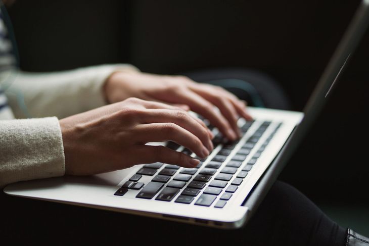 Hands typing on a laptop keyboard in a dimly lit setting
