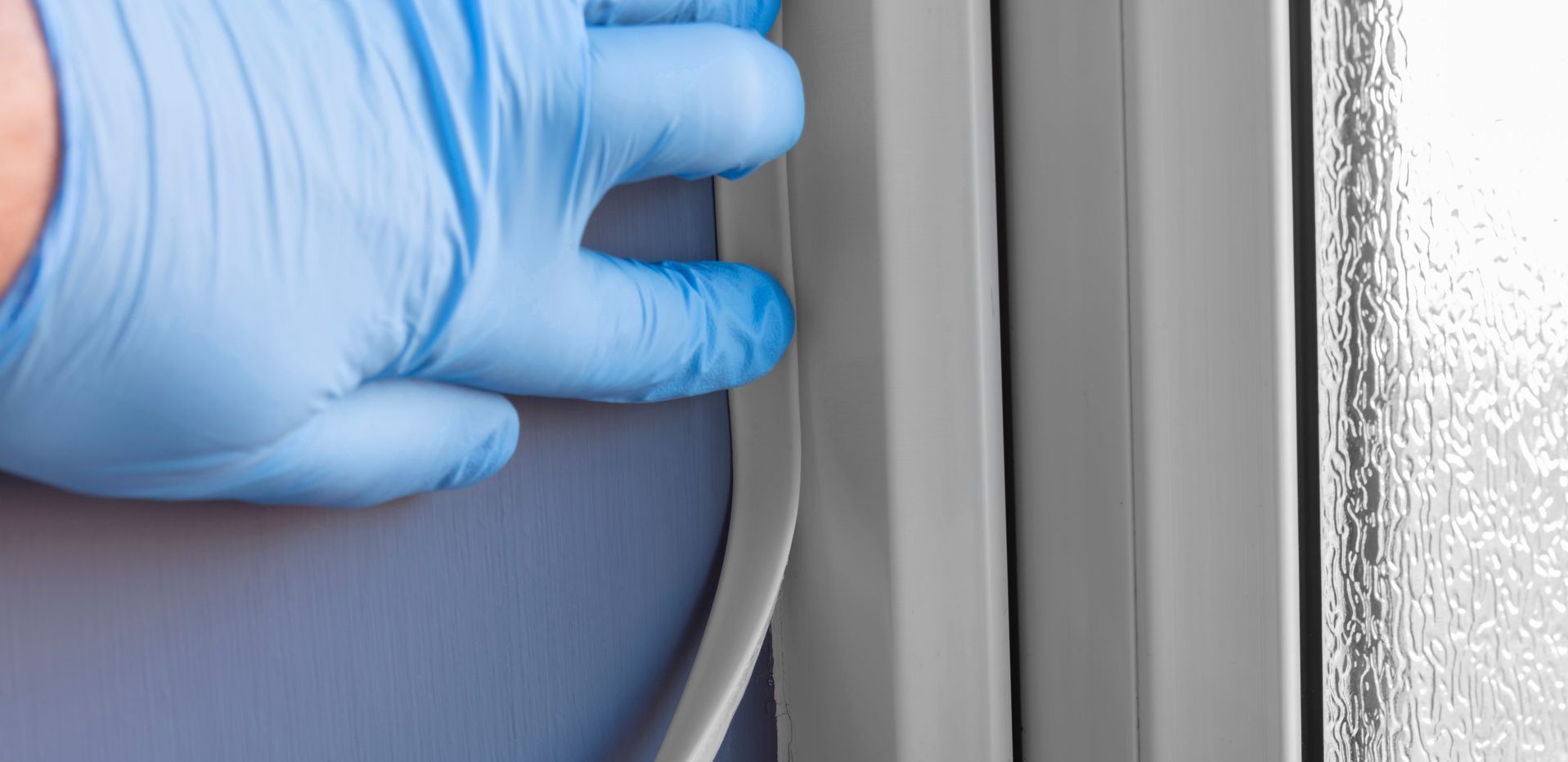 Une main gantée de bleu presse une bande blanche souple contre un cadre gris.