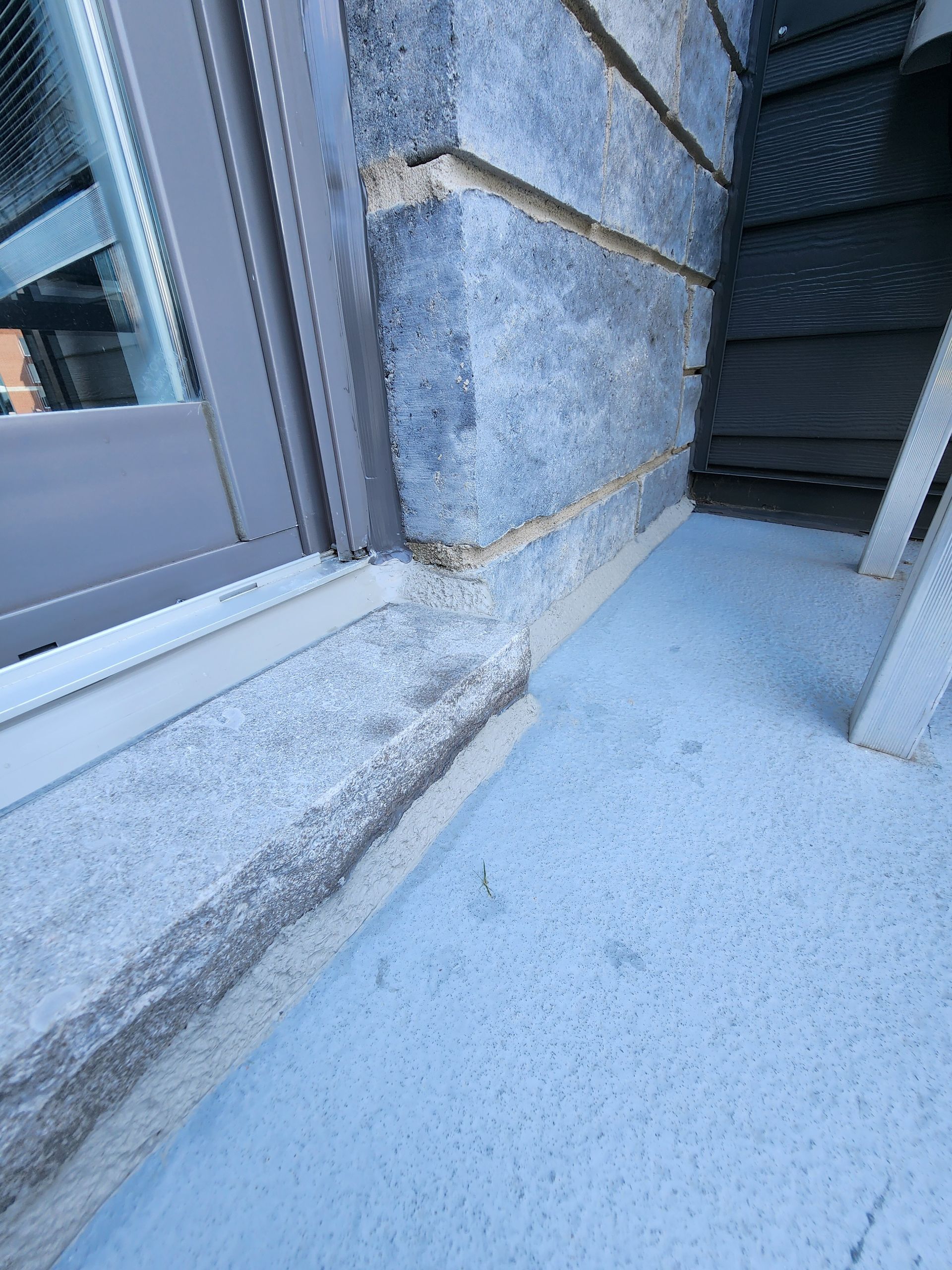 Détail d'un mur extérieur avec fenêtre, bardage gris texturé et corniche claire.