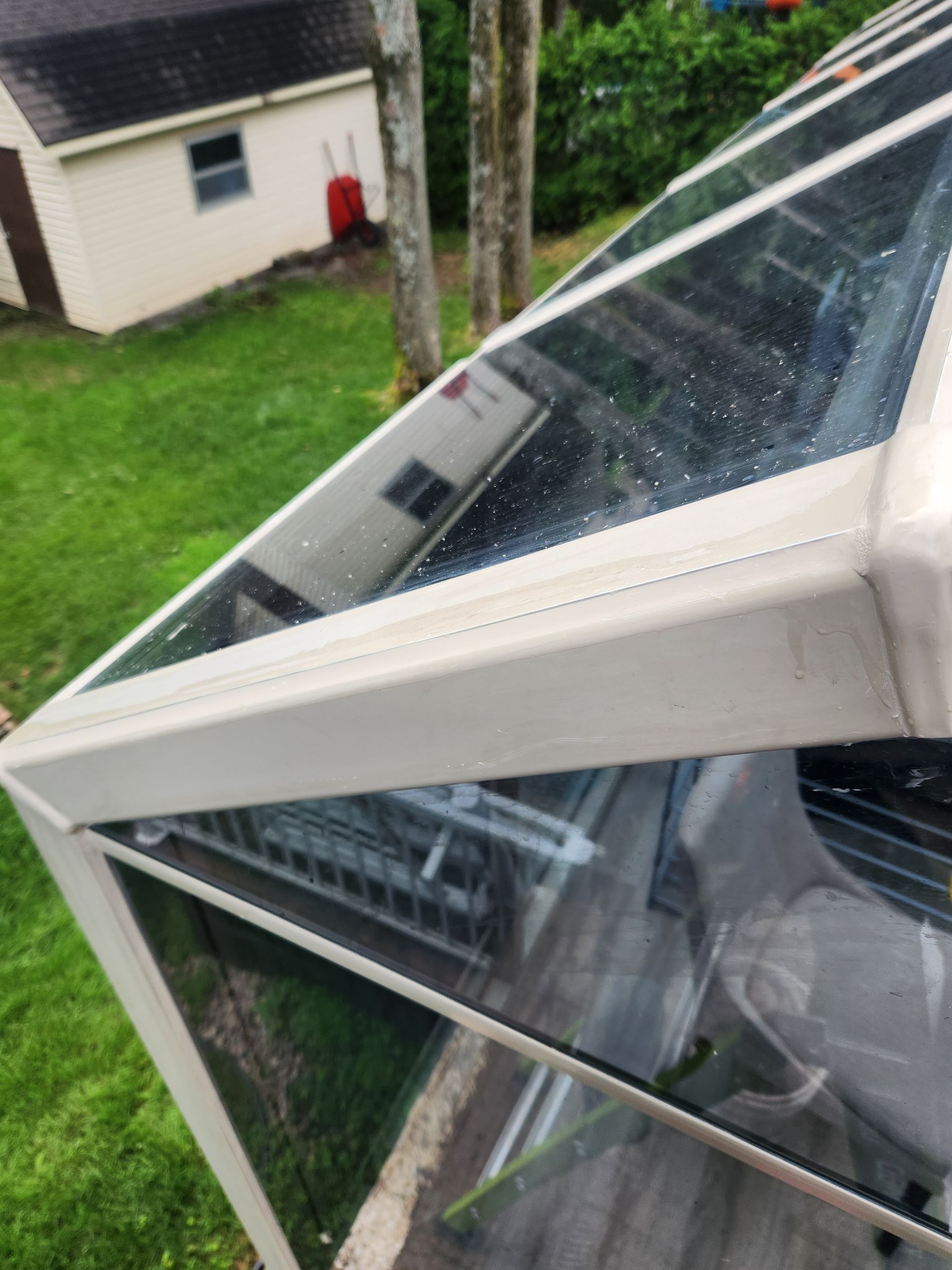 Un toit transparent avec un cadre blanc et une maison en arrière-plan