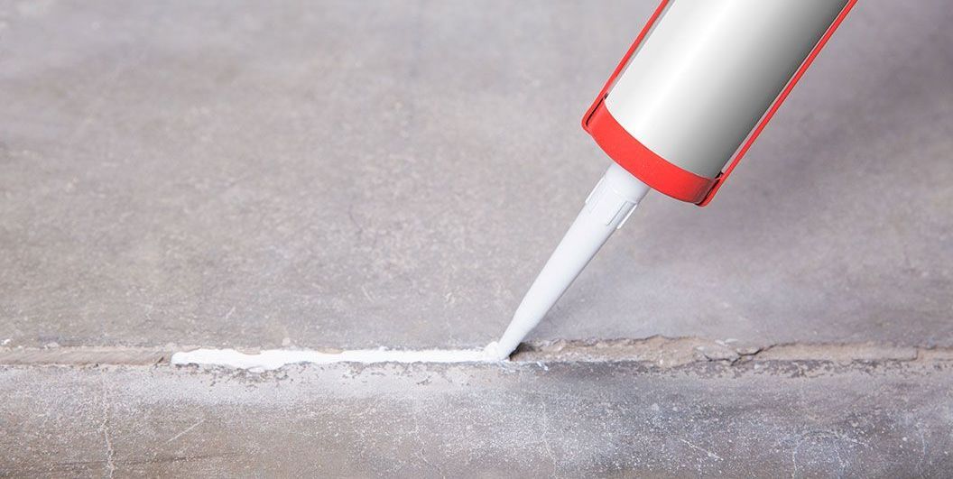 Un pistolet à calfeutrer pulvérisant du mastic blanc dans un interstice d'une surface grise.