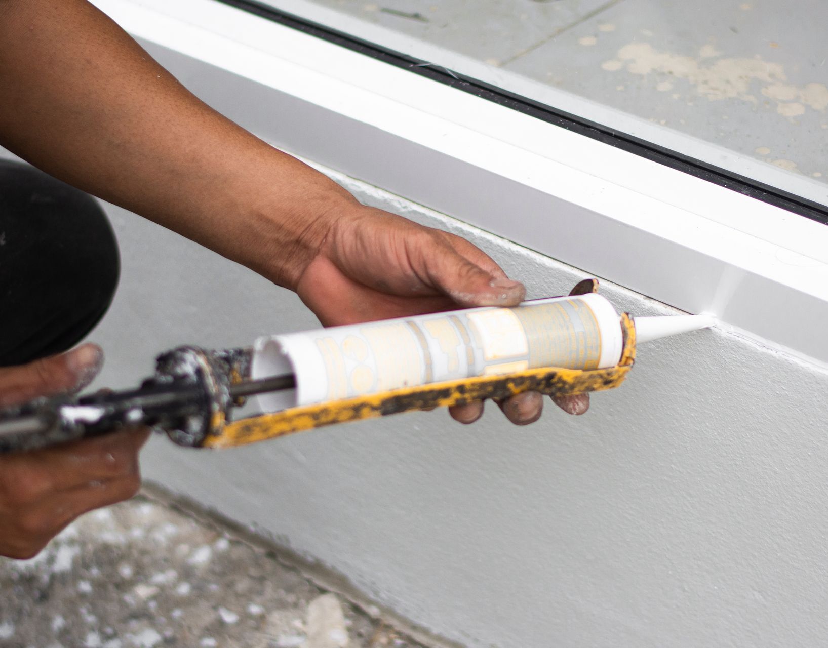 Une personne applique du mastic sur le rebord d'une fenêtre.